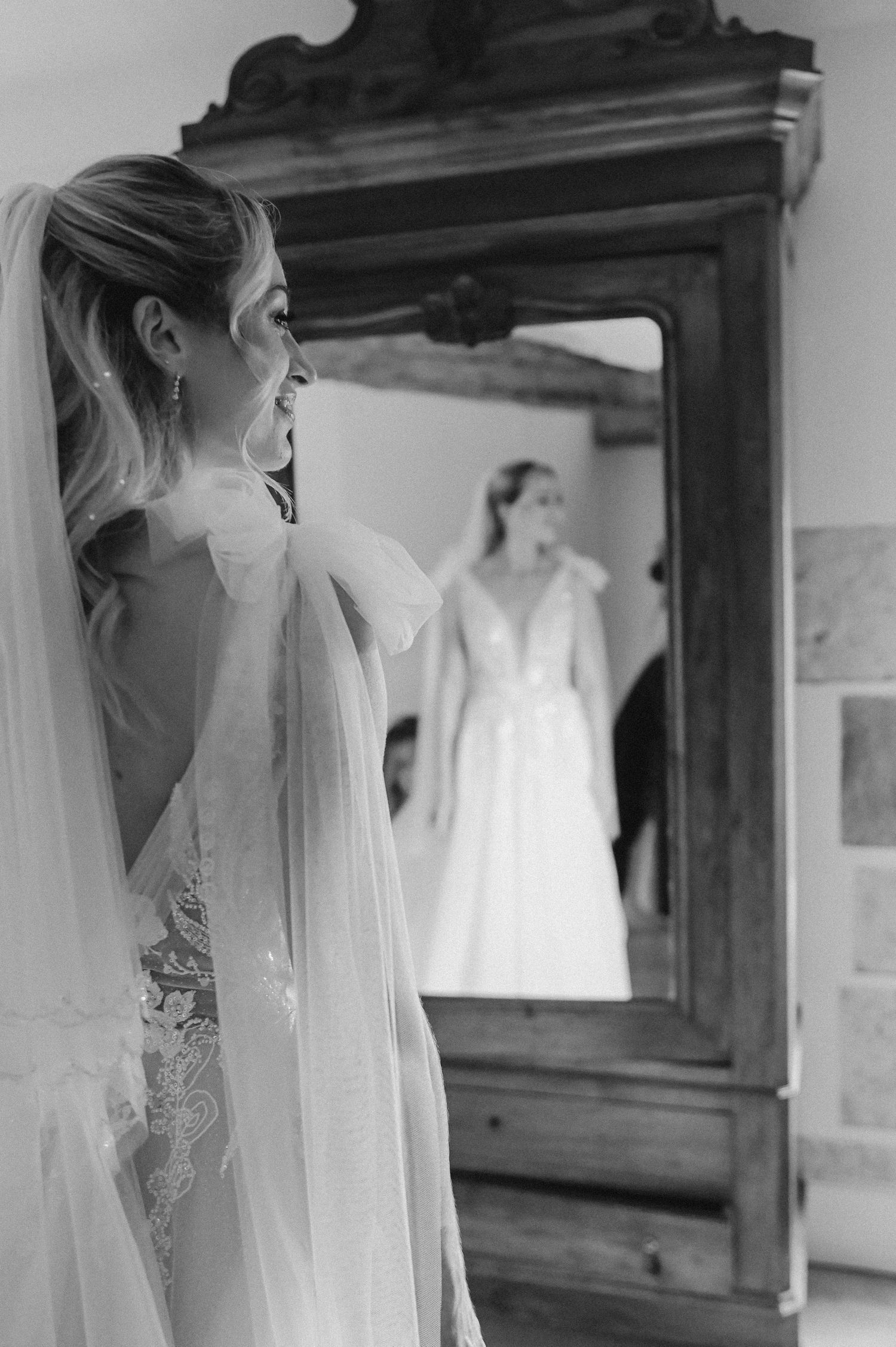Black and white portrait of a bride looking at her reflection in an antique mirror.