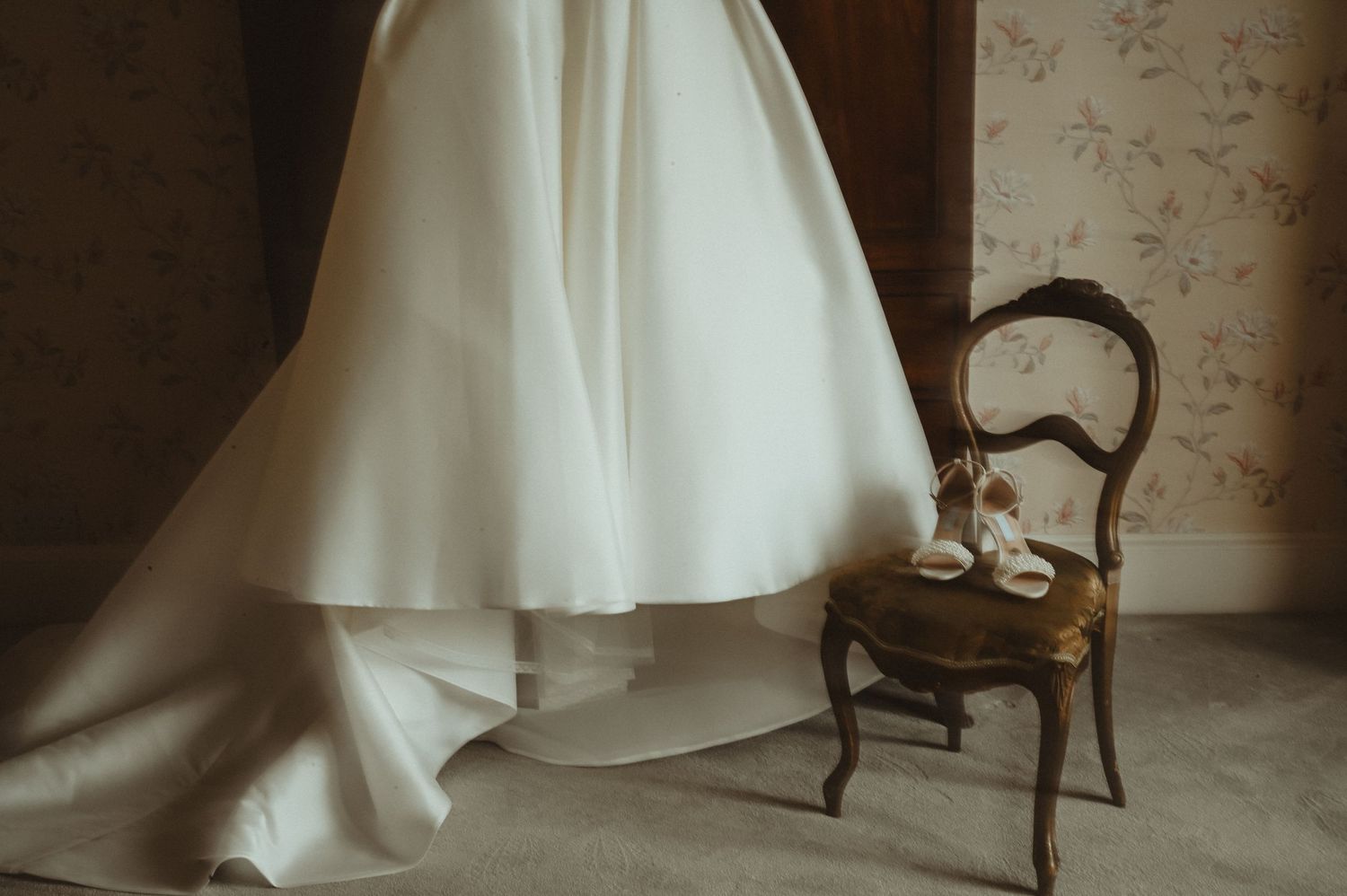 White wedding dress elegantly draped next to vintage chair in natural light.
