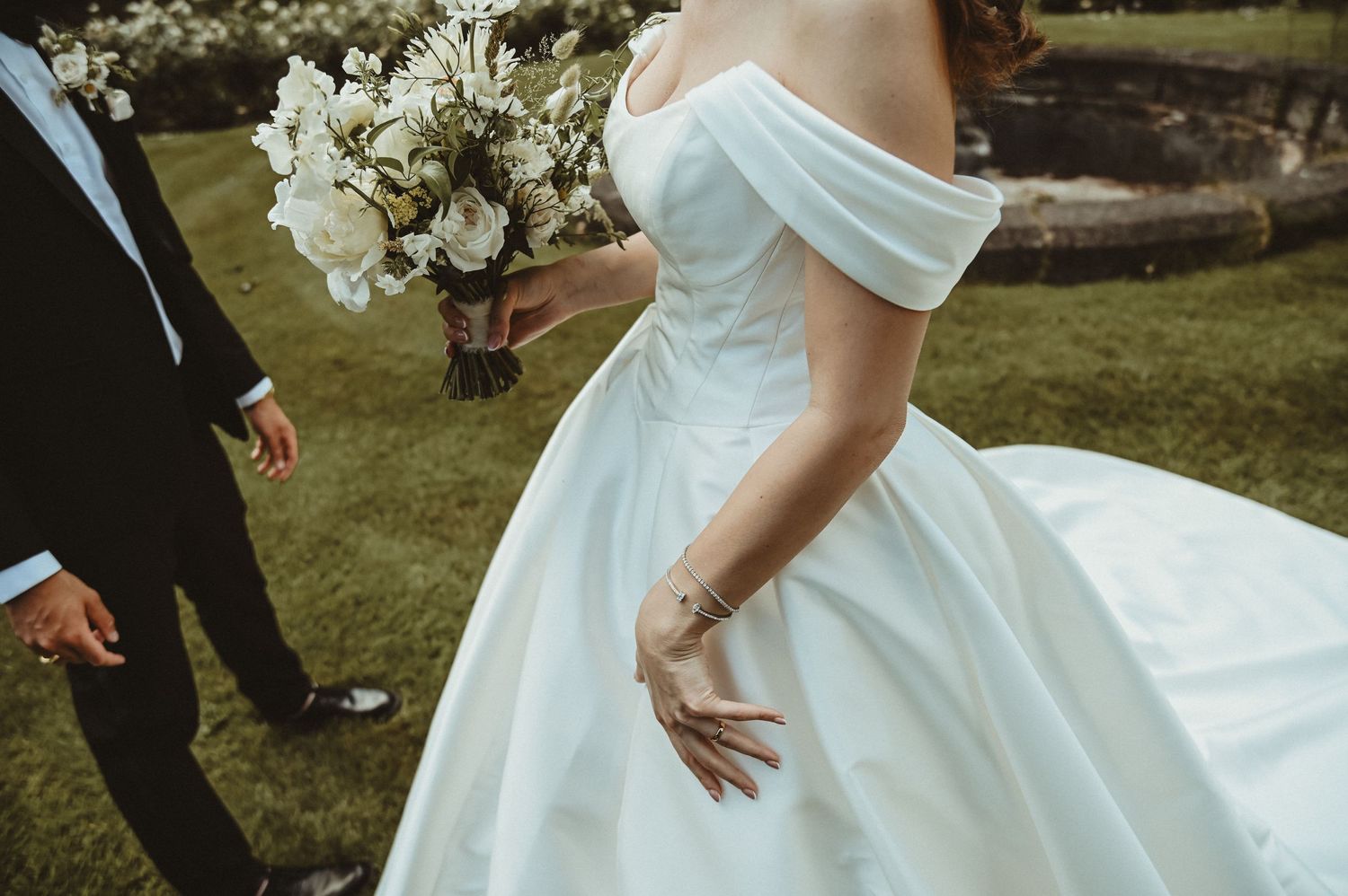 Close-up detail of an elegant off-shoulder wedding dress and white floral bouquet.