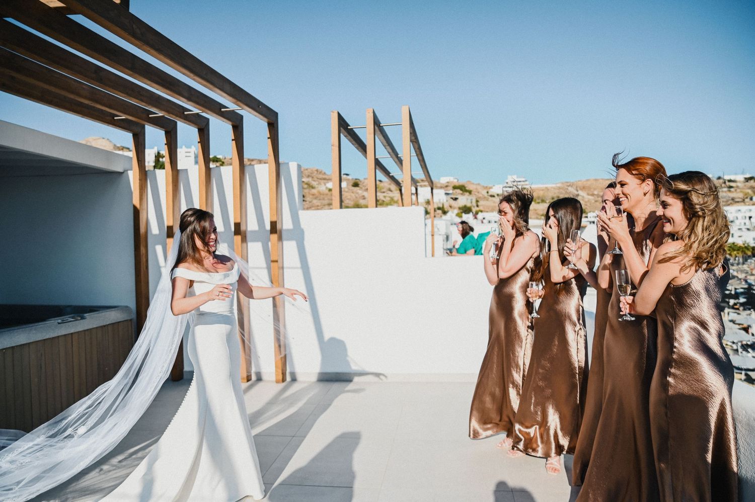 Wedding party reacting emotionally to seeing bride in her dress on sunny rooftop venue.