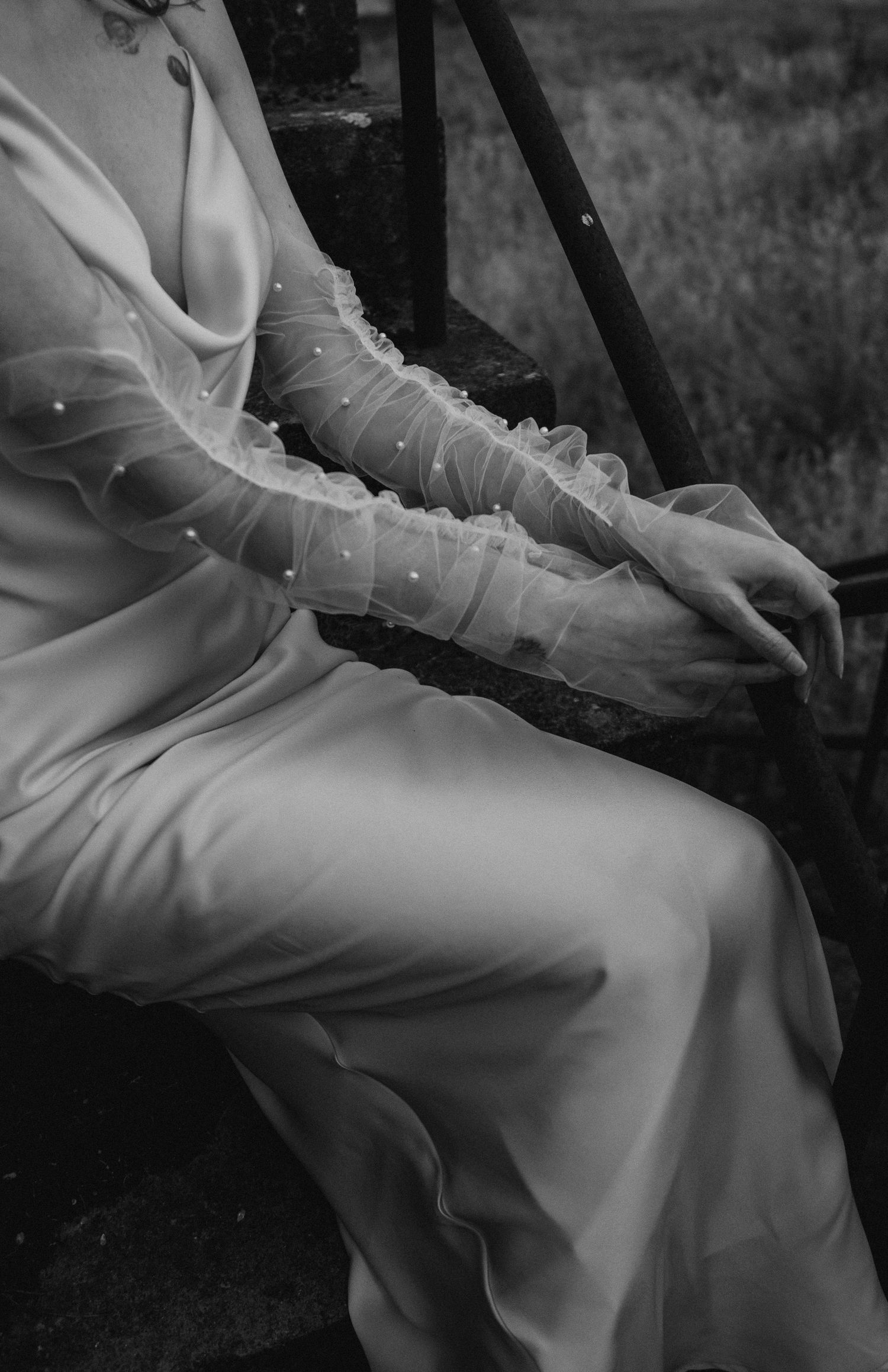 Detail shot of flowing white wedding dress with sheer pearl-adorned sleeves.