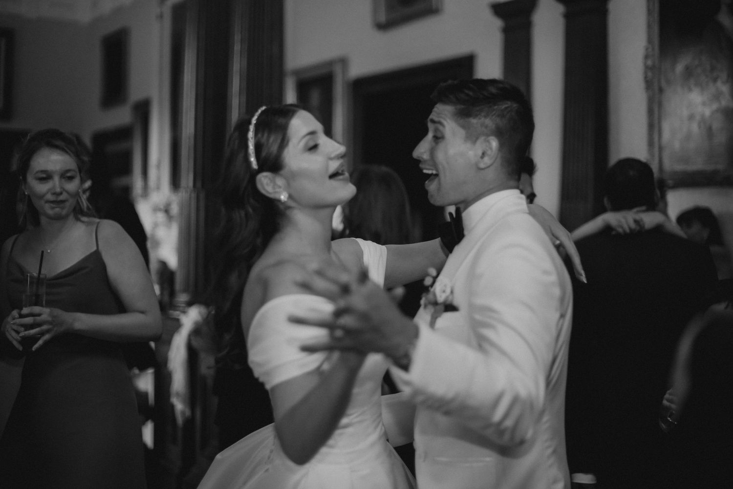 A couple dances together at an elegant indoor reception in black and white.