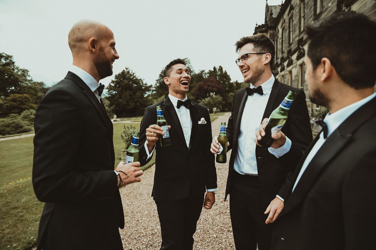 Group of formally dressed guests sharing drinks and laughter at an outdoor event.