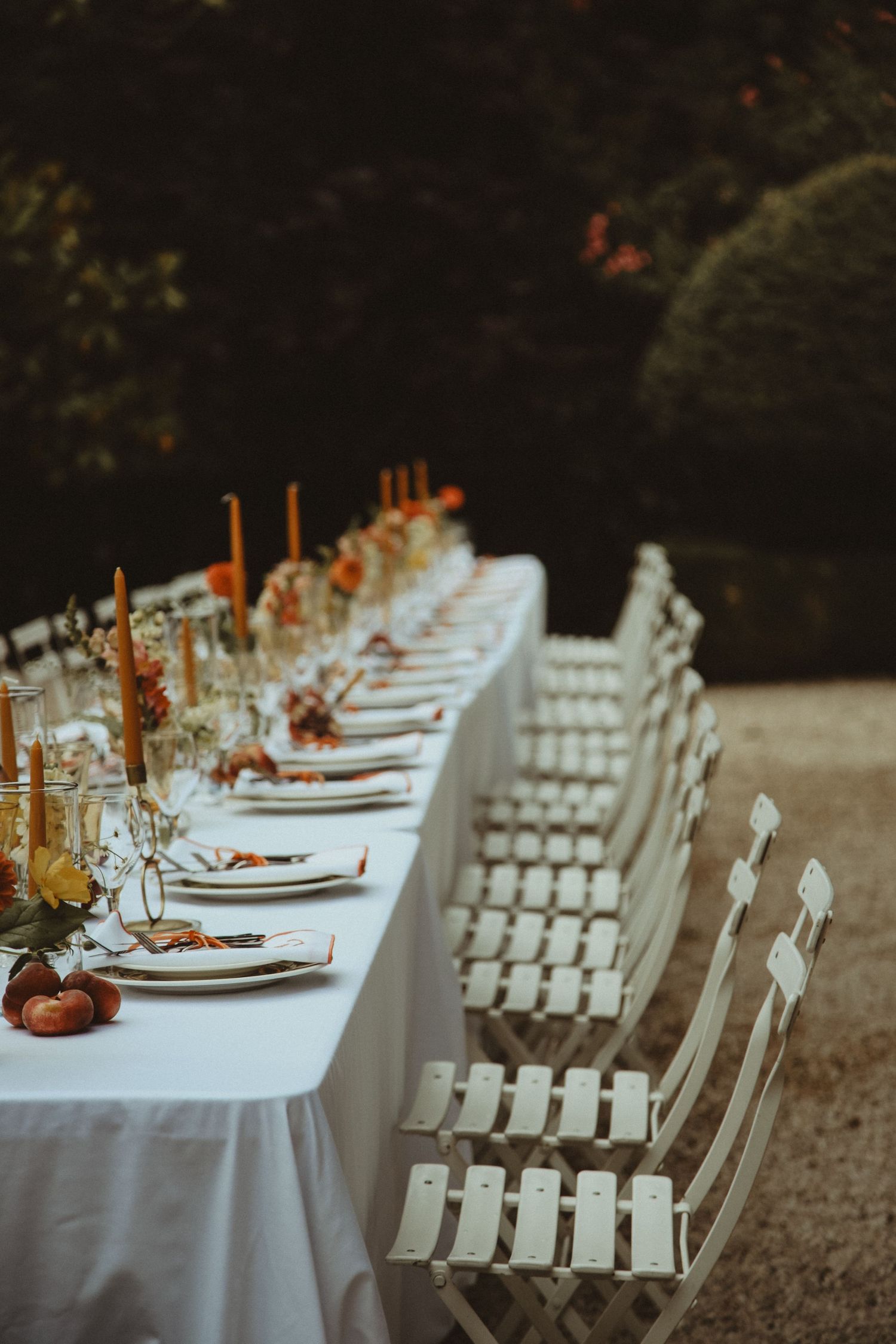Rustic wedding table setting with white chairs and orange candle centerpieces.