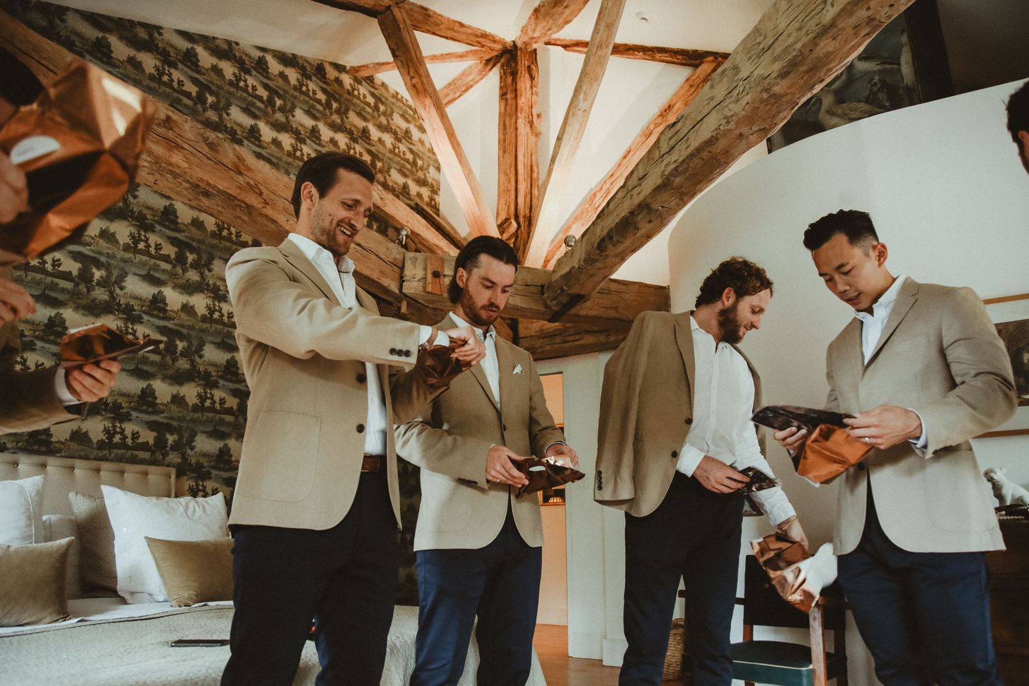 Four people in suits prepare together in a room with stone walls and wooden ceiling beams.