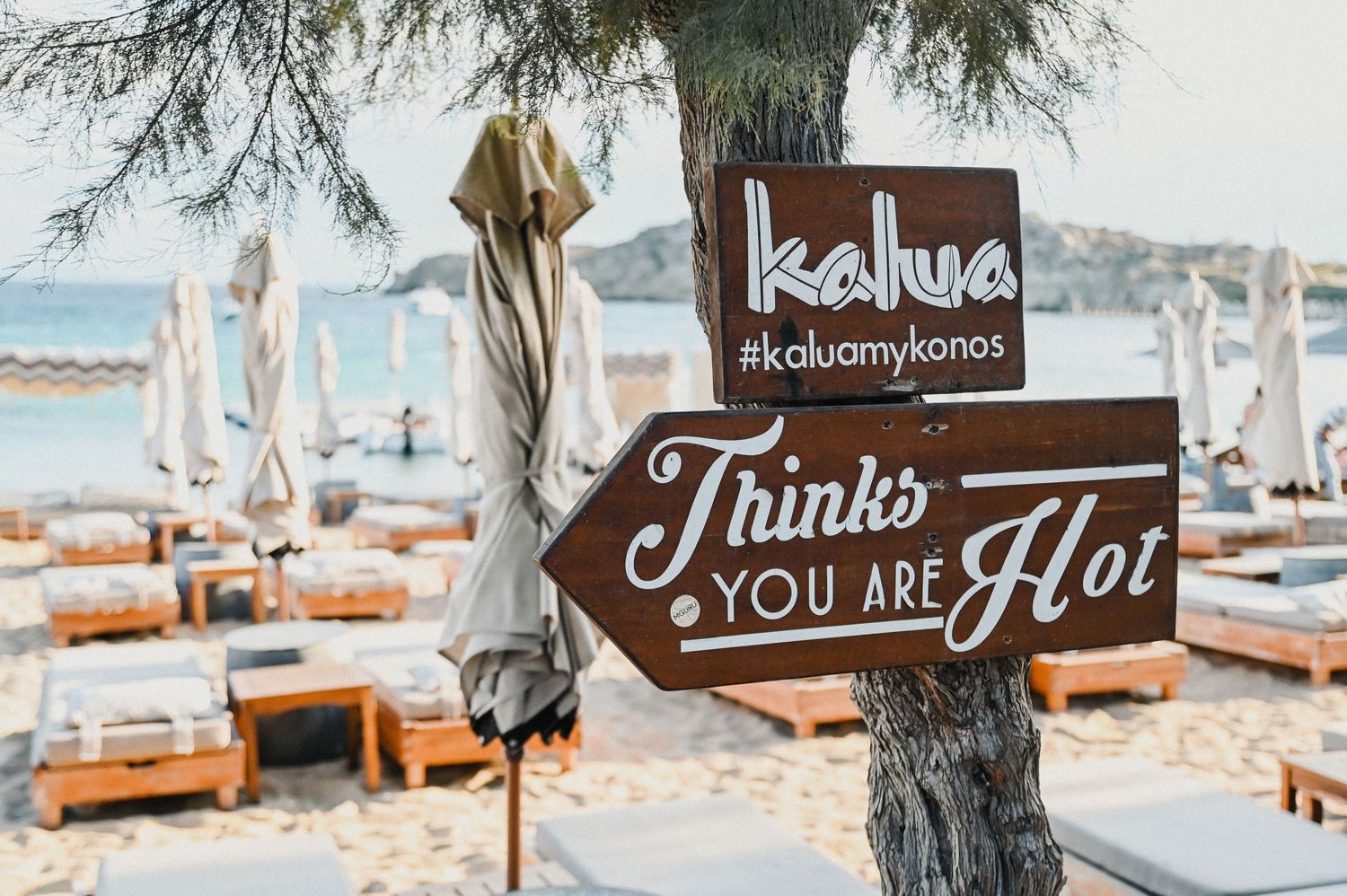 Wooden sign reading 'Thinks You're Hot' with Kahlua branding at beach wedding setup.