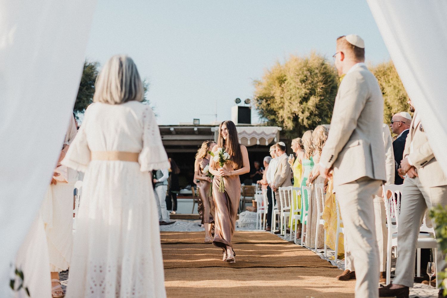 Wedding ceremony processional on wooden deck with guests in light summer attire.
