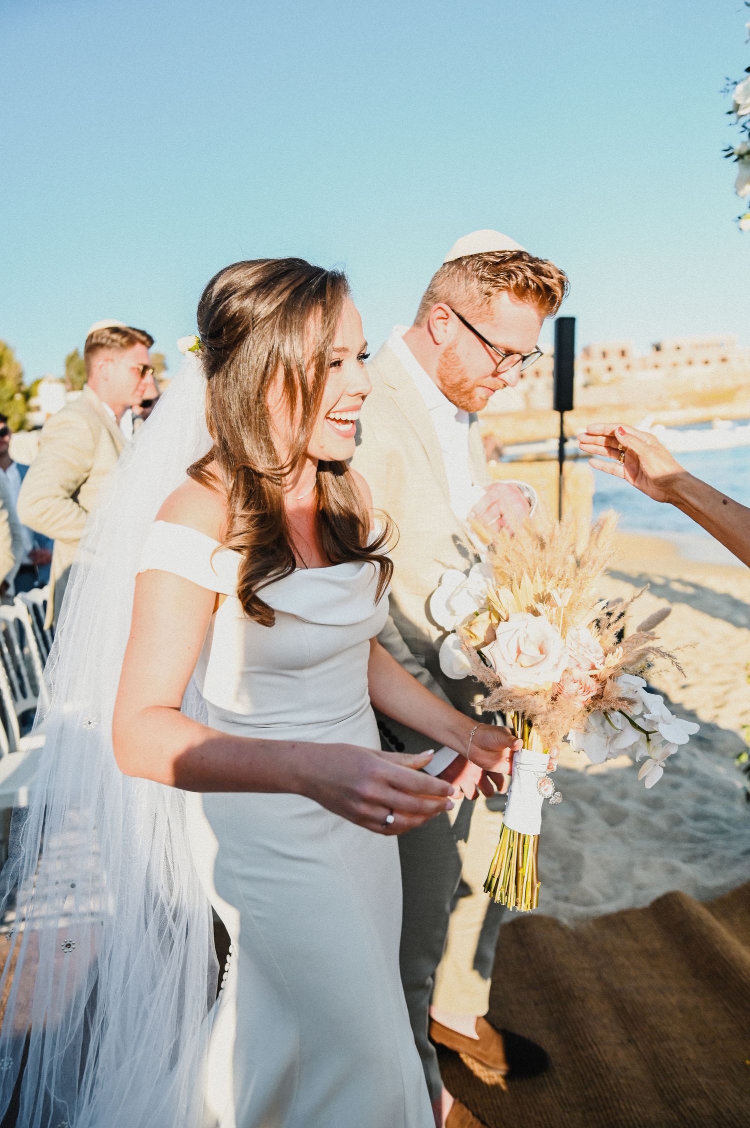 Seaside wedding celebration with elegant white dress and dried flower bouquet.