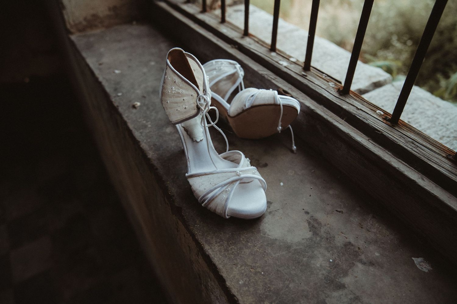 White strappy bridal sandals positioned on rustic windowsill.