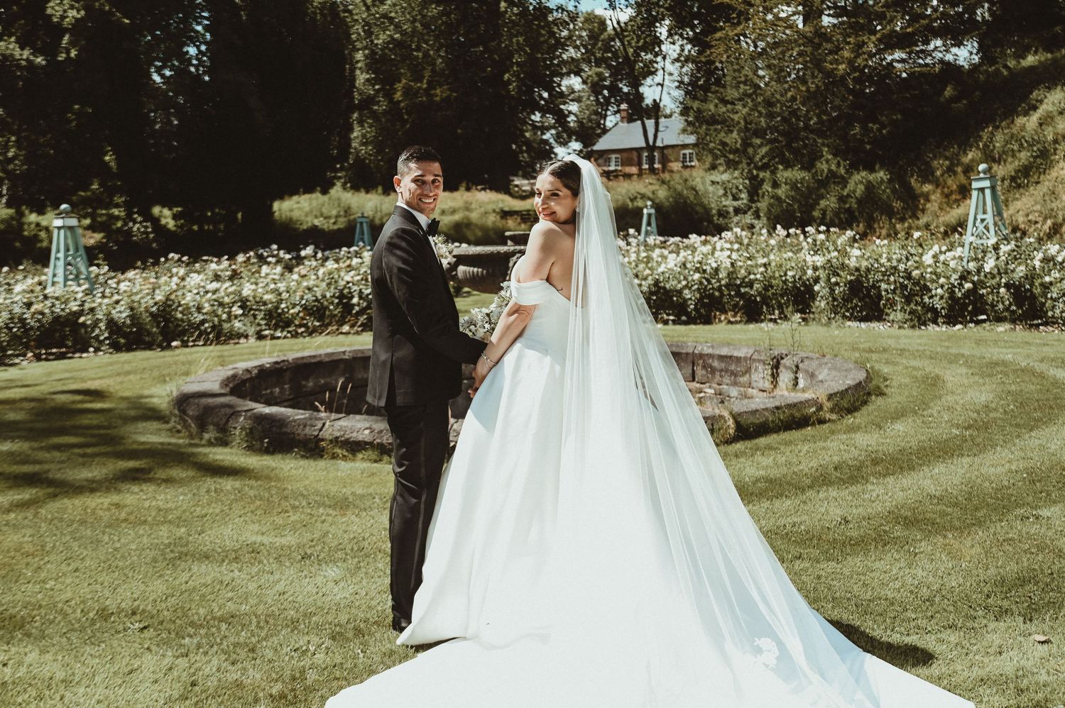 A stunning wedding scene in a manicured garden with a long flowing white dress train.