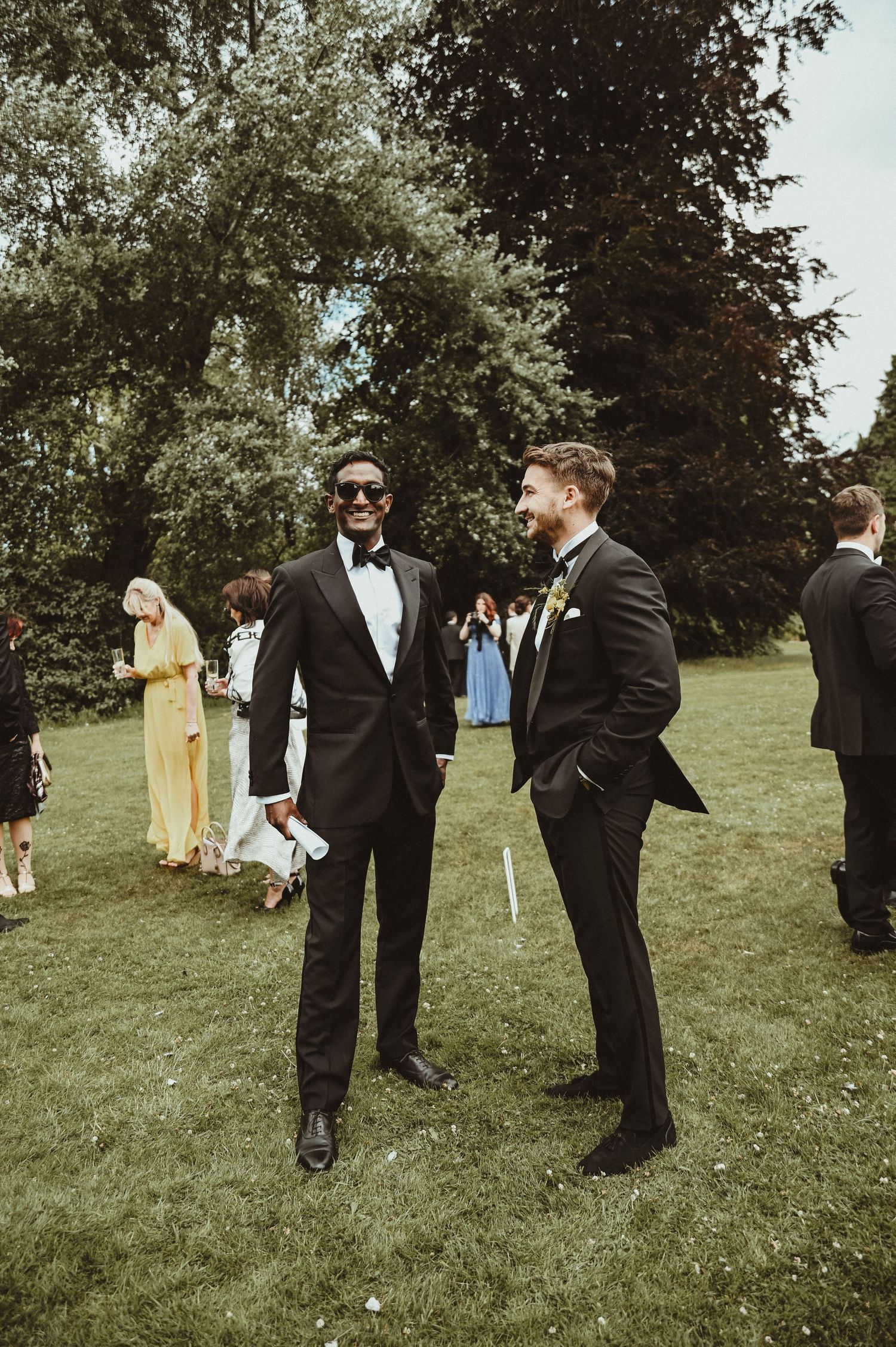 Two guests in formal attire engage in conversation on the lawn during an outdoor wedding reception.