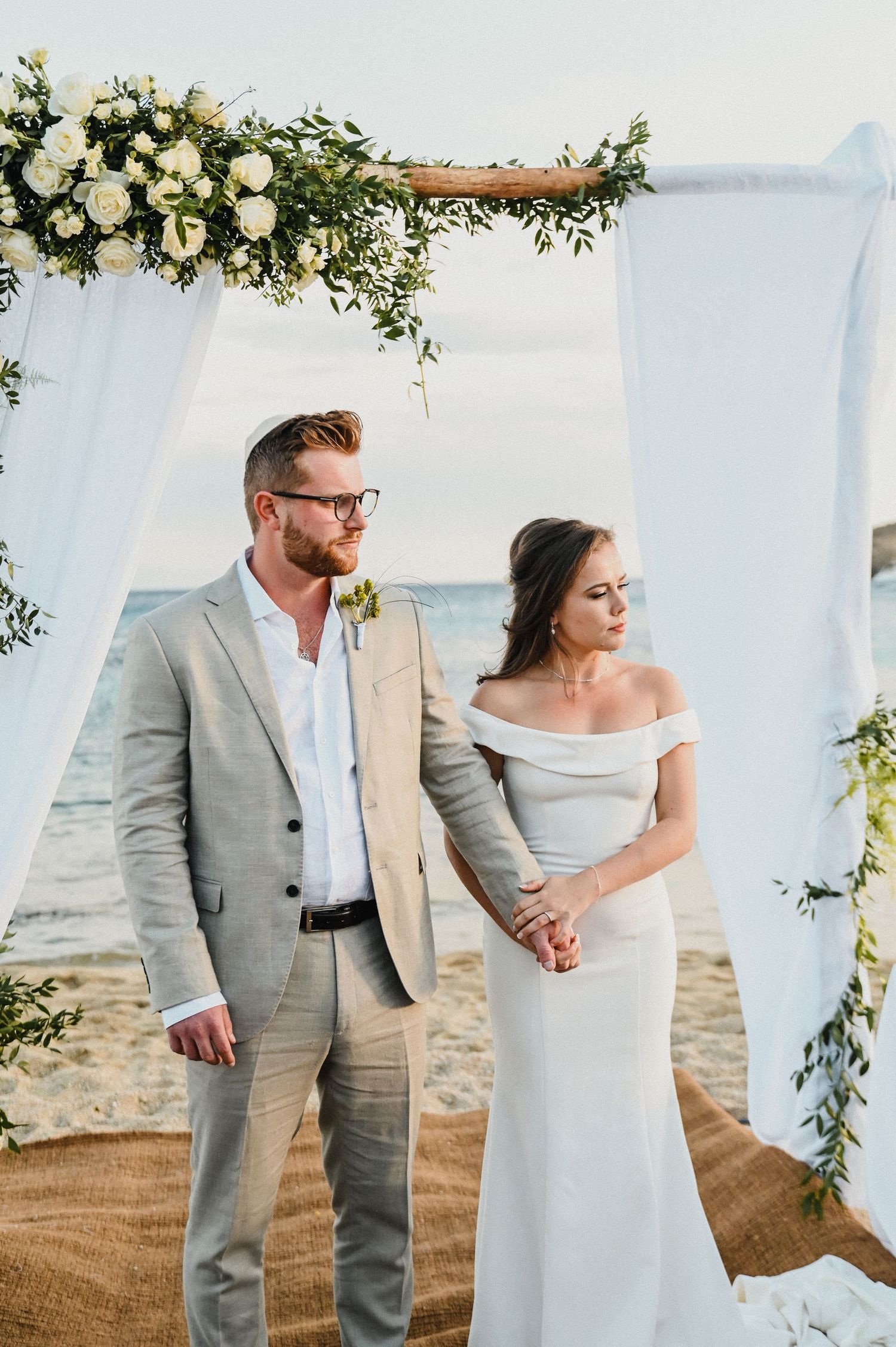 Newlyweds stand together under floral arch during beachside ceremony.