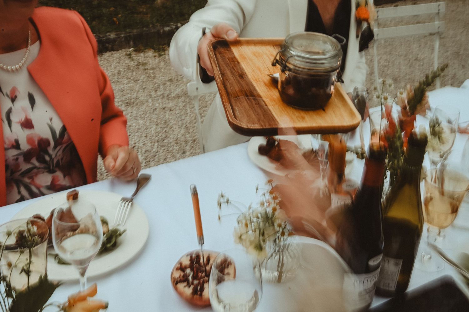 Wooden serving board with drinks and appetizers on an elegant table setting.