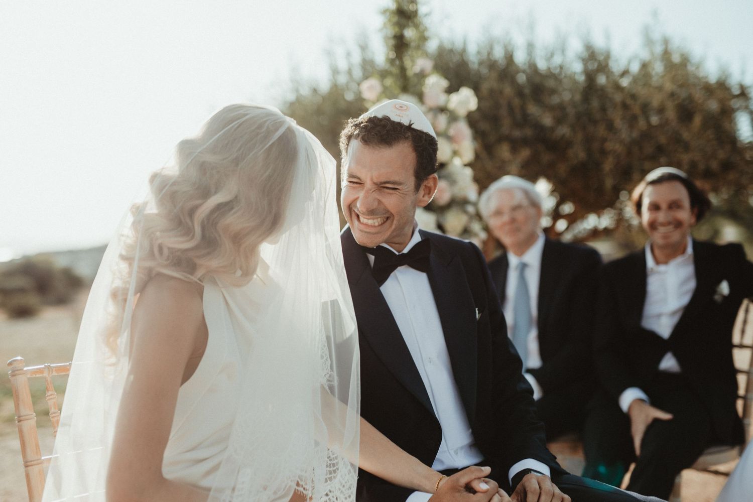 Wedding ceremony moment captured in bright sunlight with natural landscape backdrop.