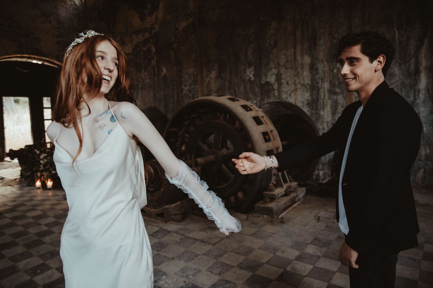 A couple shares a playful moment in an abandoned industrial space with vintage machinery.