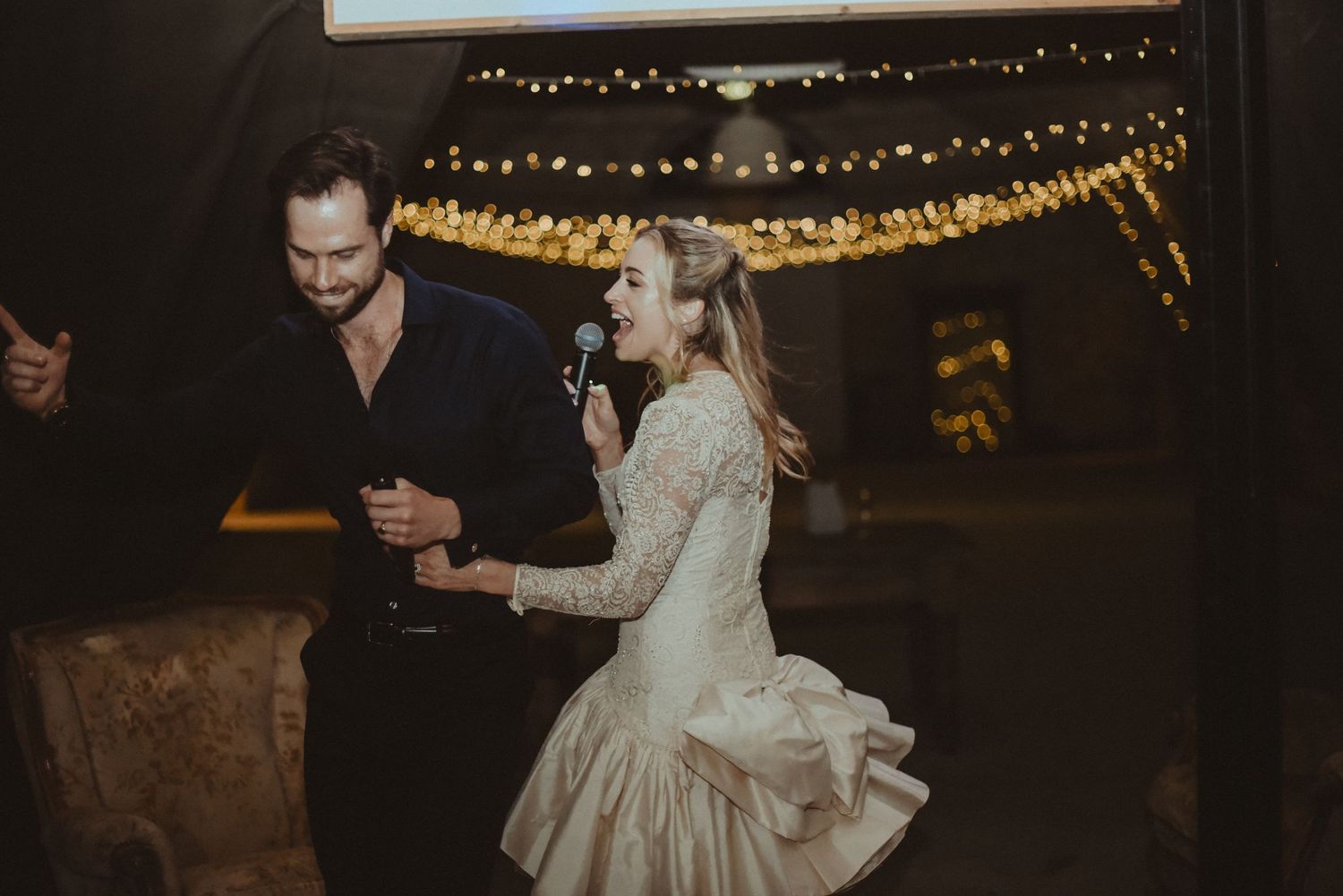 A couple dancing in a vintage-style dress at an intimate wedding reception with string lights.