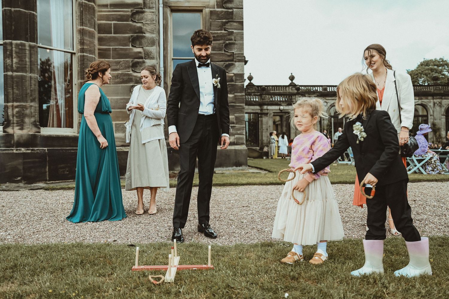 Wedding guests play lawn games outside stone building during reception.