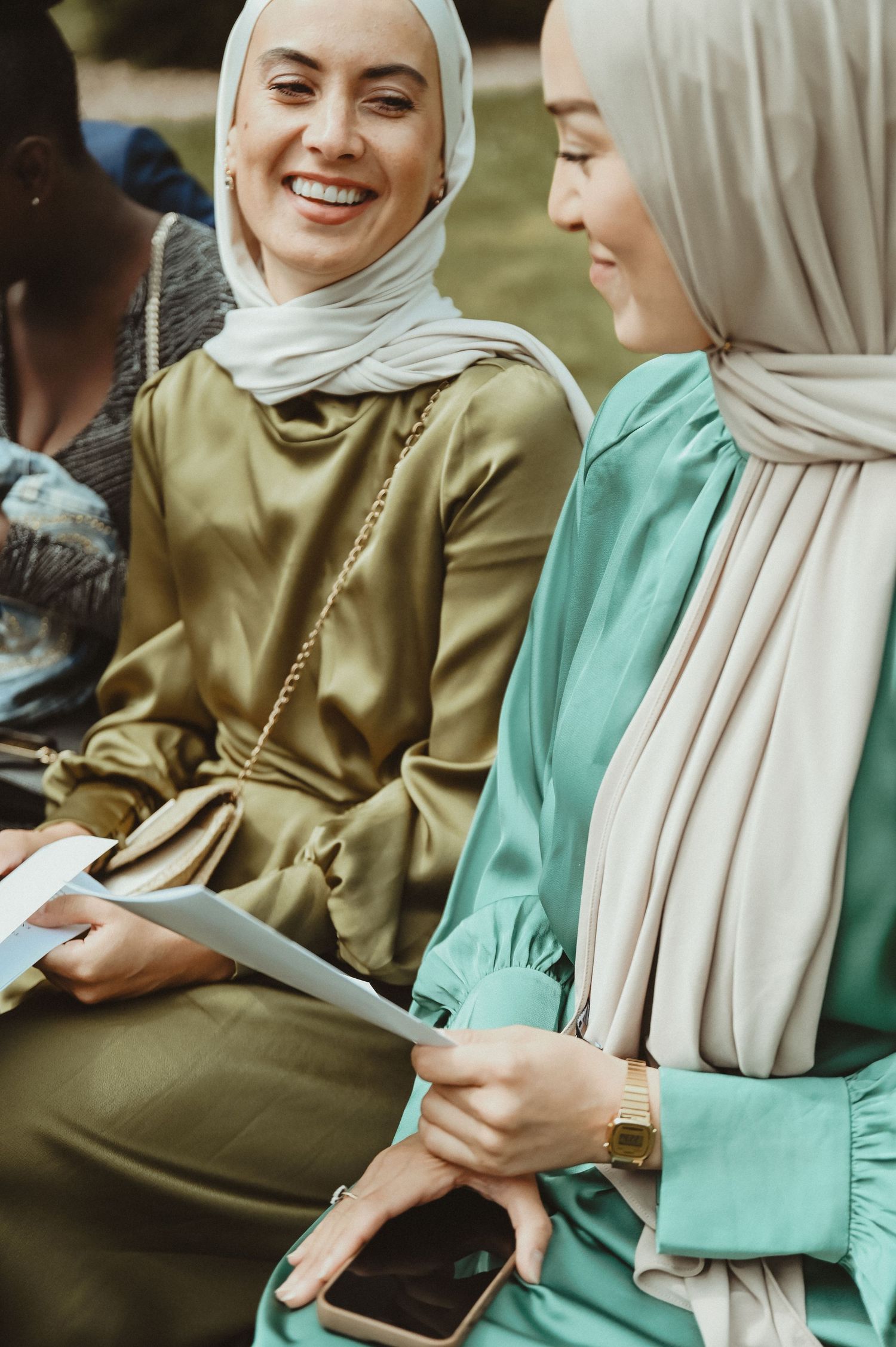 Two women in elegant modest dress sharing a moment while looking at a tablet.