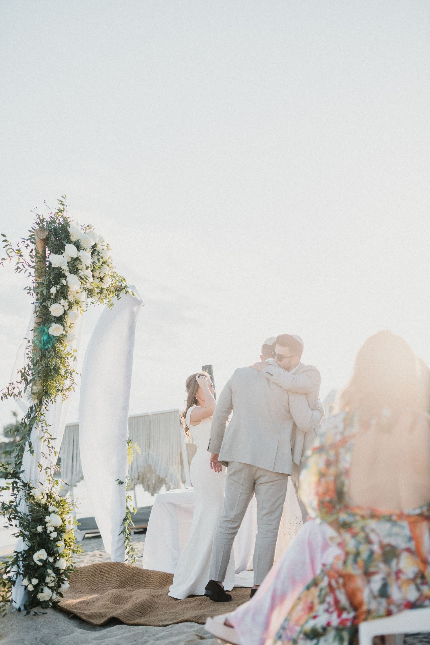 Wedding ceremony under floral arch with soft sunlight and white draping.