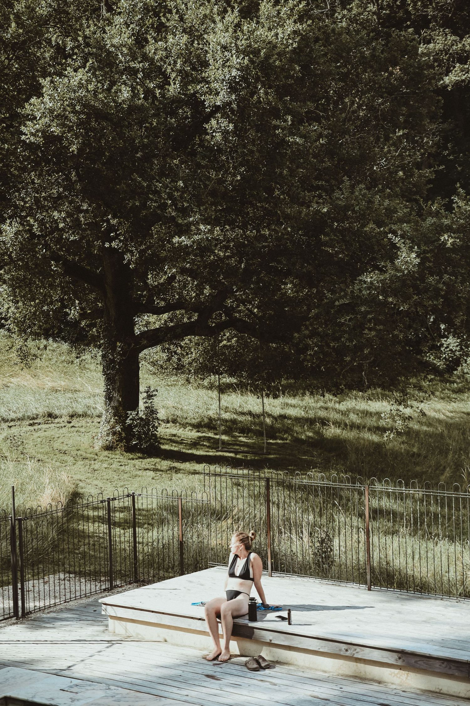 Person sitting on white platform beneath large tree in outdoor setting.