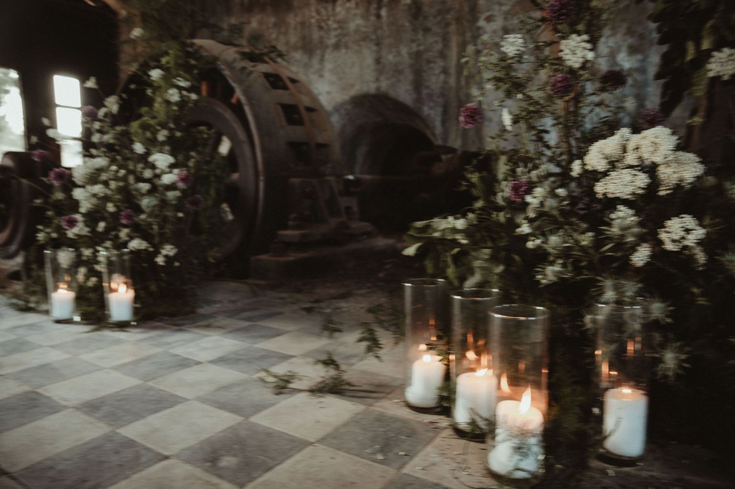 Moody wedding venue with rustic machinery, floral arrangements and glowing candles.
