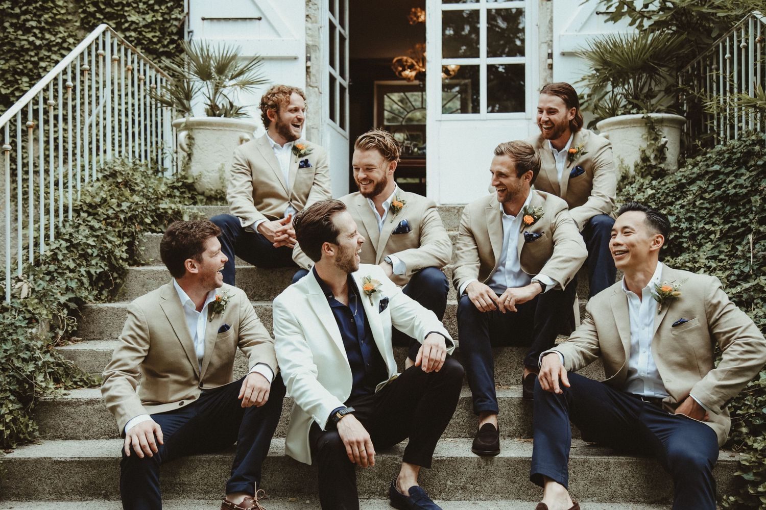 Wedding party relaxes and laughs on outdoor steps in casual group photo.