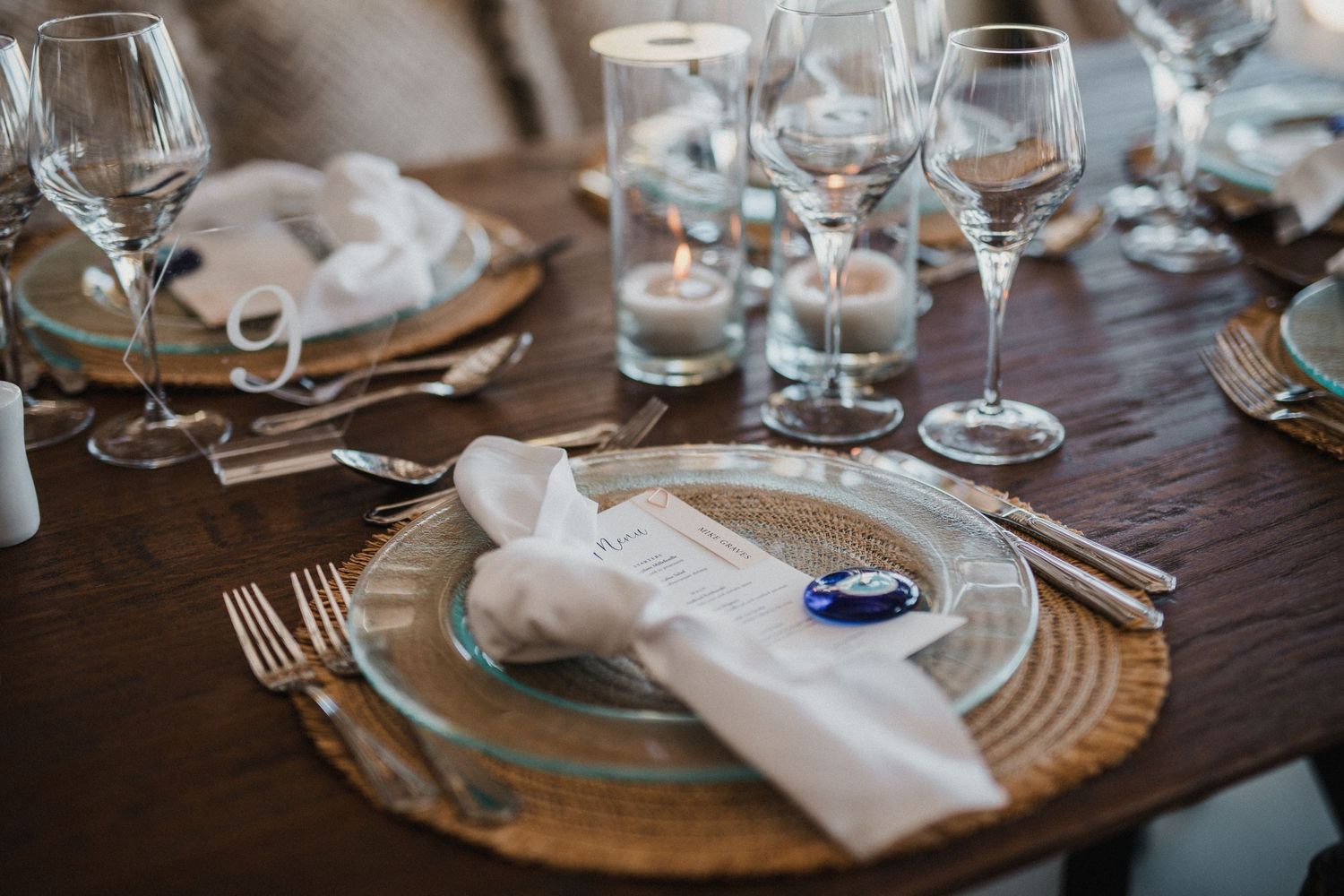 Elegant place setting with gold charger plate, white napkin, and wine glasses on dark table.