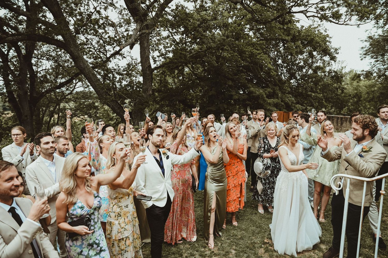 Wedding guests celebrate and applaud during an outdoor garden ceremony.