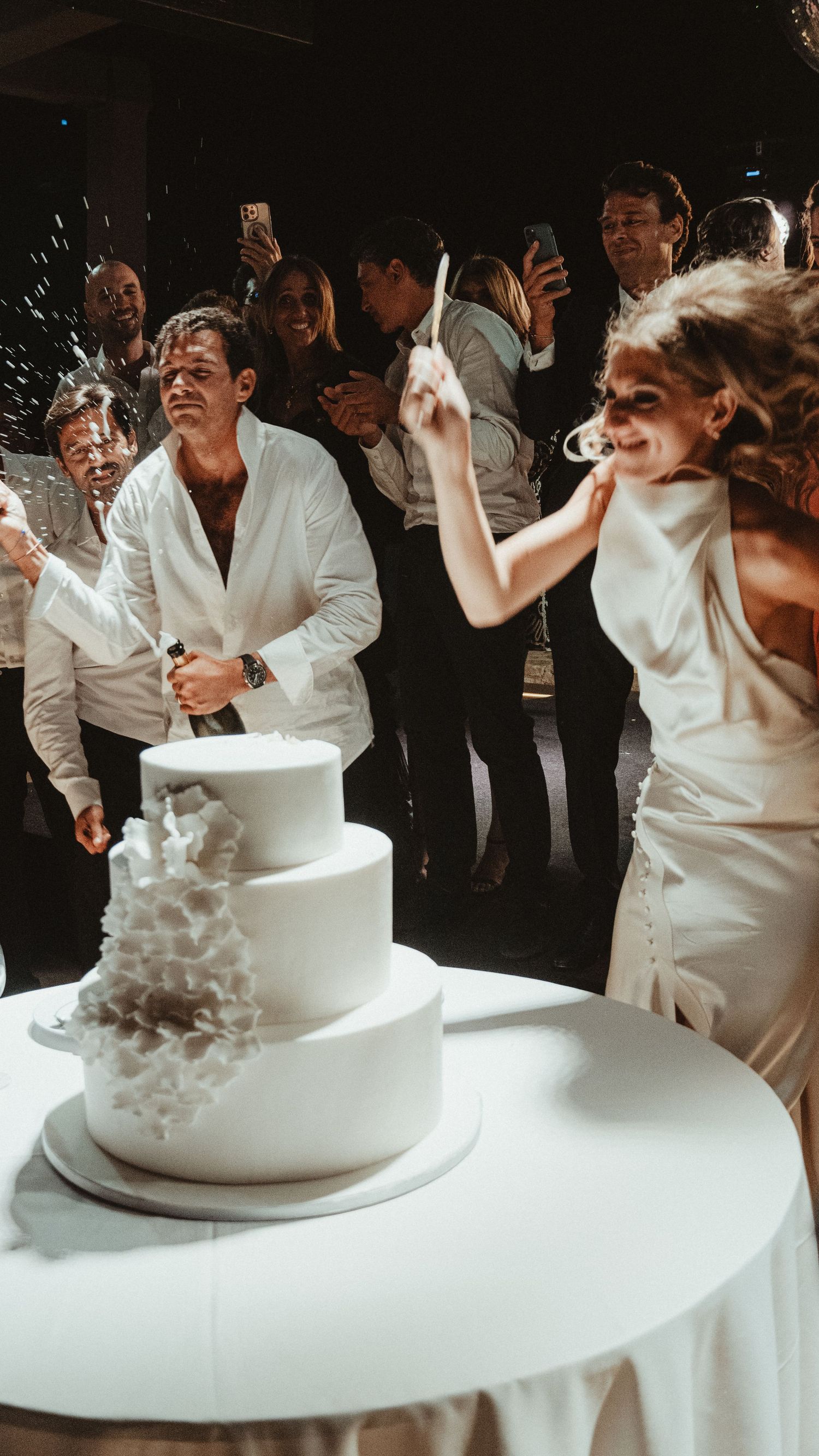 Wedding celebration moment with couple cutting cake while guests cheer and celebrate.