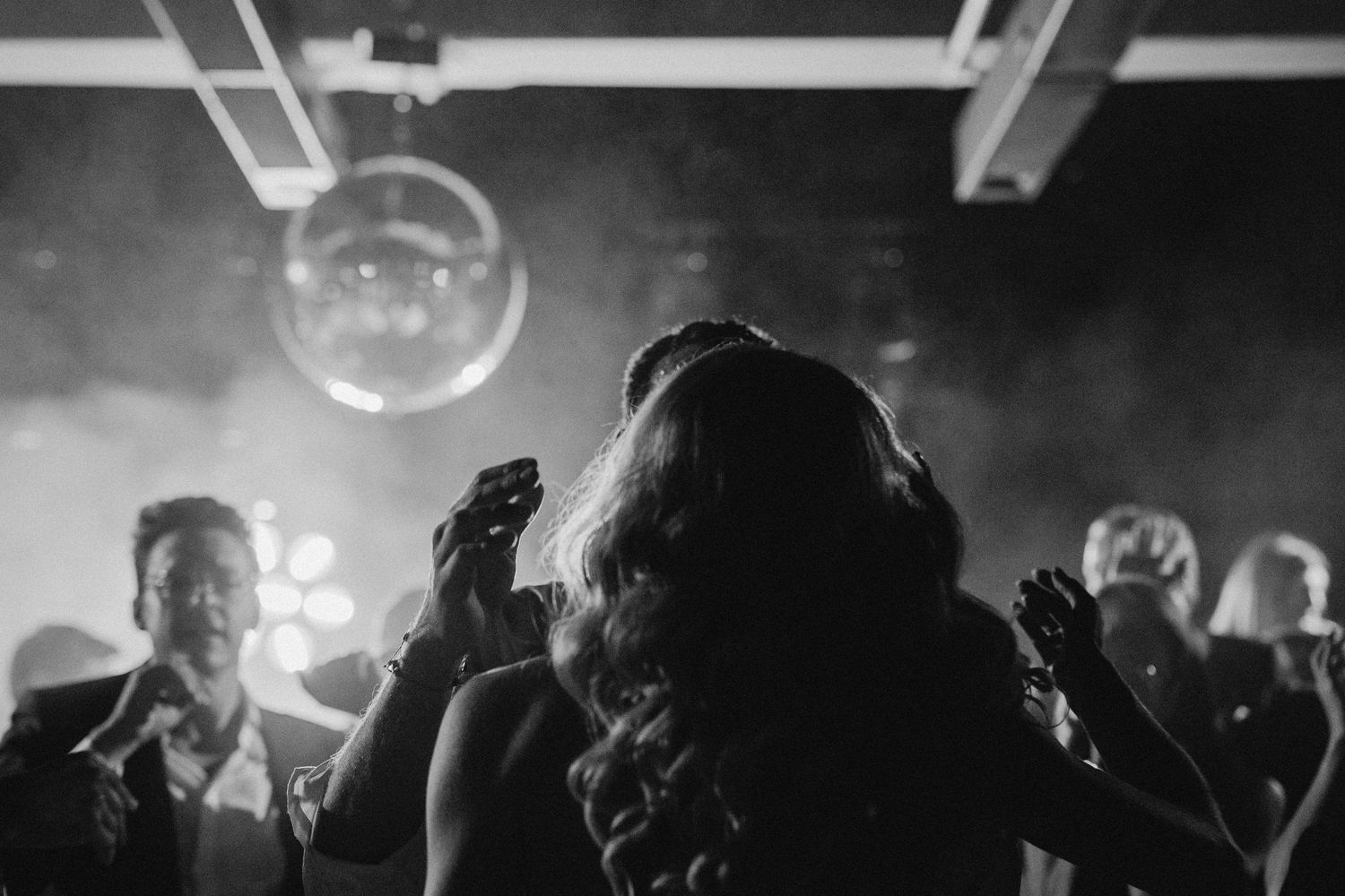 Silhouettes of people dancing under a disco ball in smoky atmosphere.