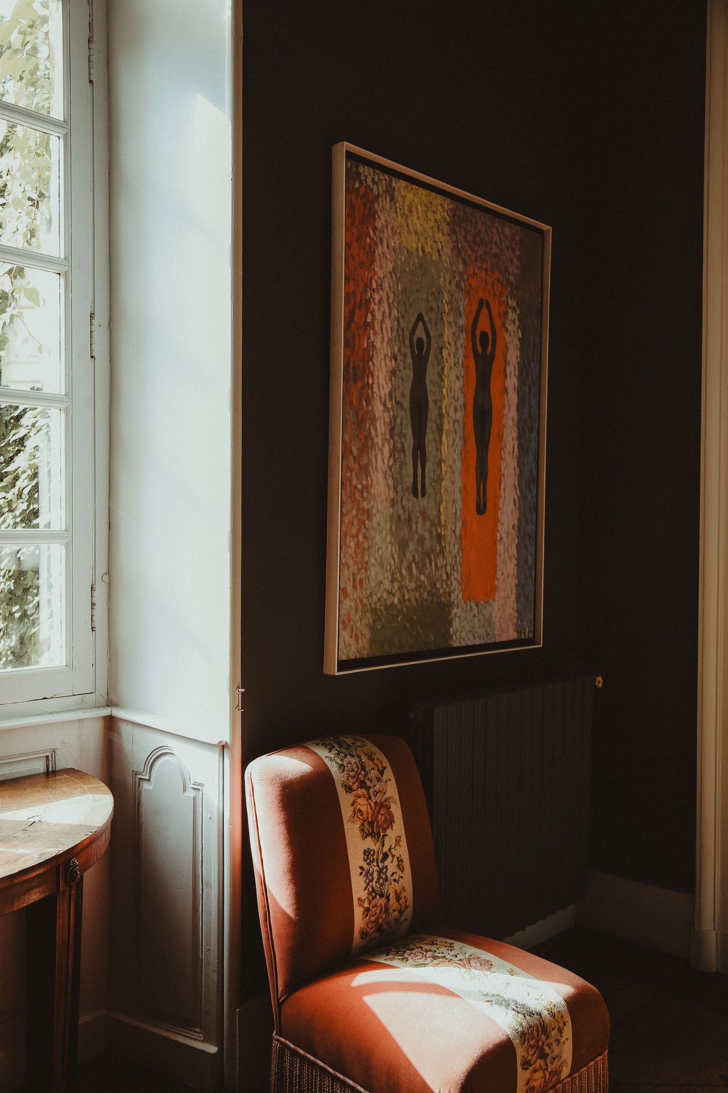 Vintage orange armchair and abstract wall art in corner of room with large window.
