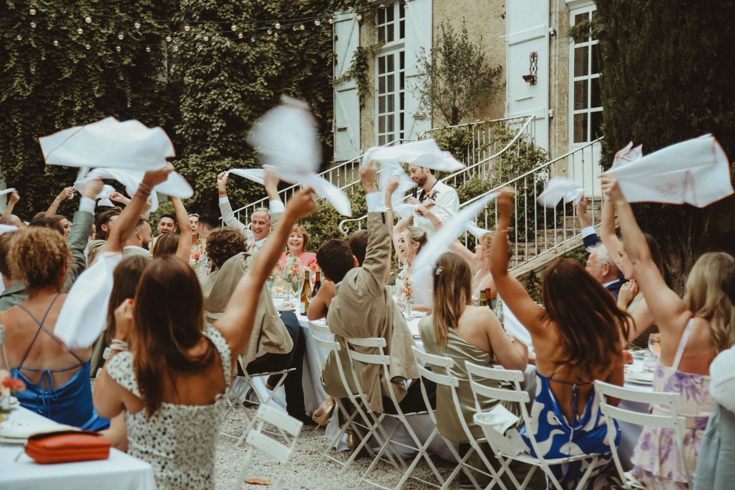 Wedding guests celebrating with napkin wave during outdoor reception dinner.