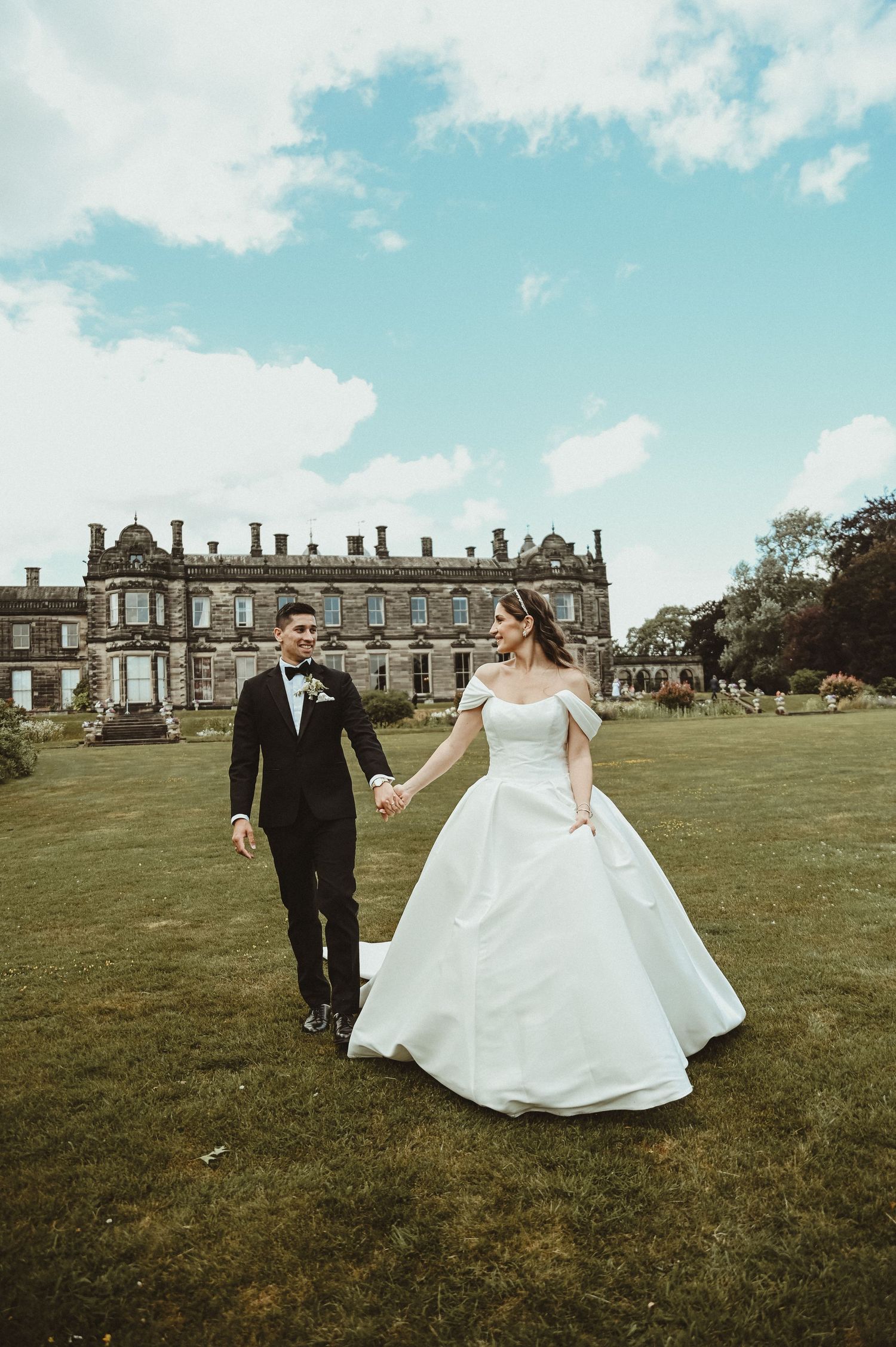 Newlyweds walk hand in hand across grand estate lawn on their wedding day.