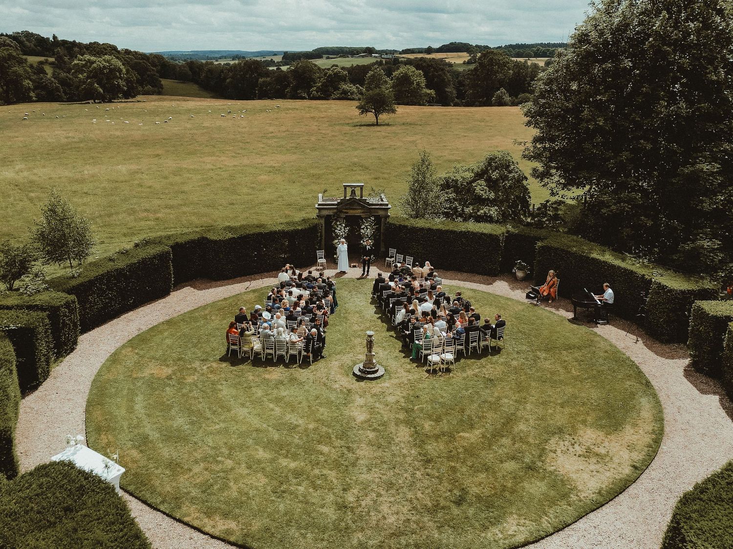 Aerial view of circular outdoor wedding ceremony setup surrounded by countryside landscape.