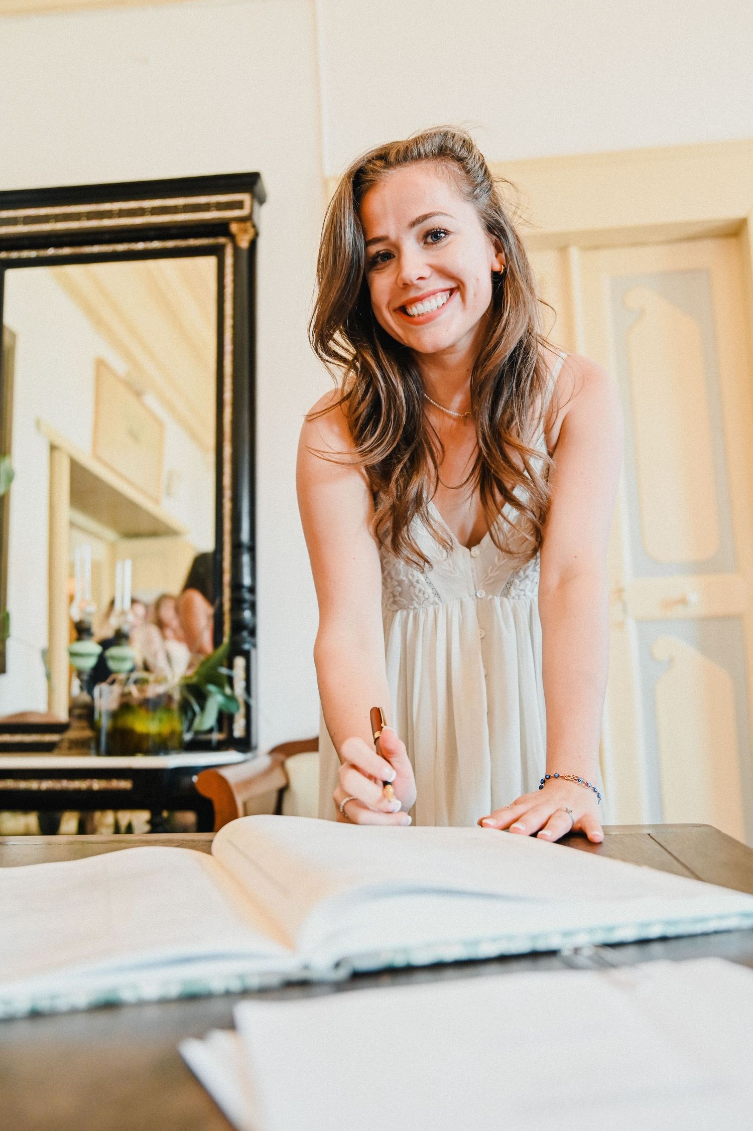A person in a light-colored dress leans over a book on a table.
