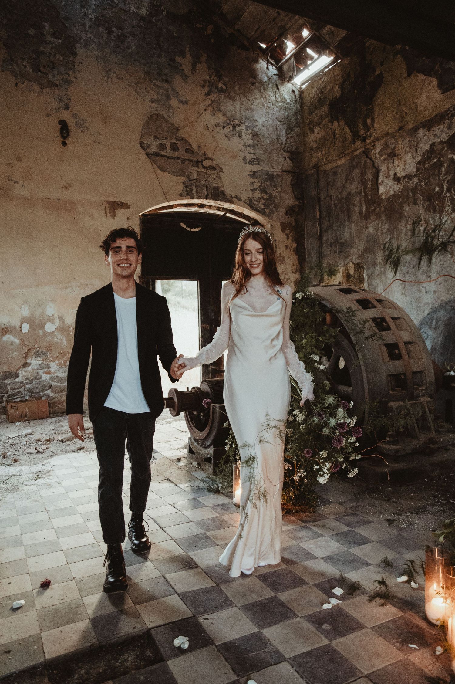 A stylish couple walks through an atmospheric industrial venue with checkered floors and vintage machinery.