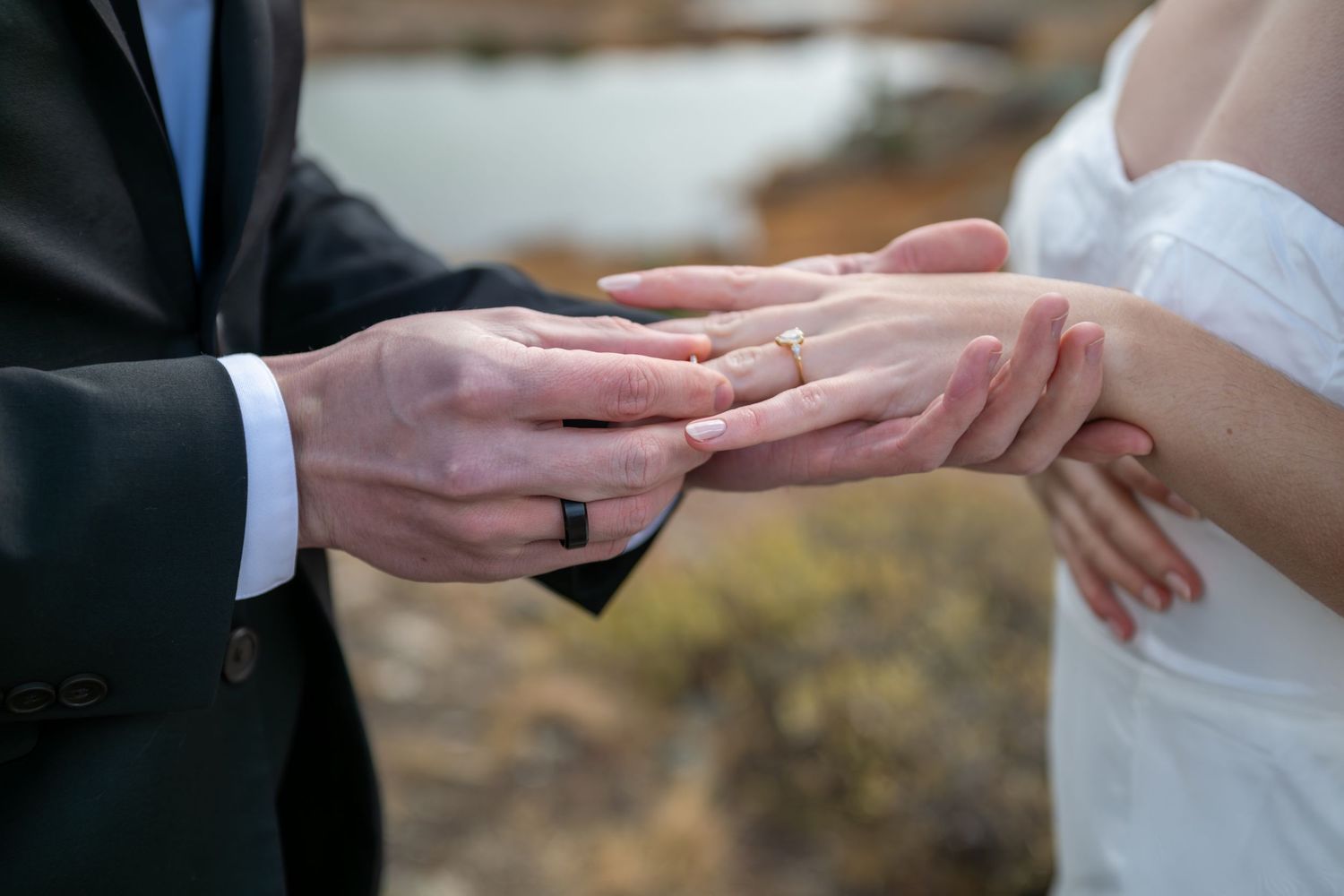 A detail image of a groom placing a gold wedding ring on brides finger during an outdoor elopement wedding ceremony.