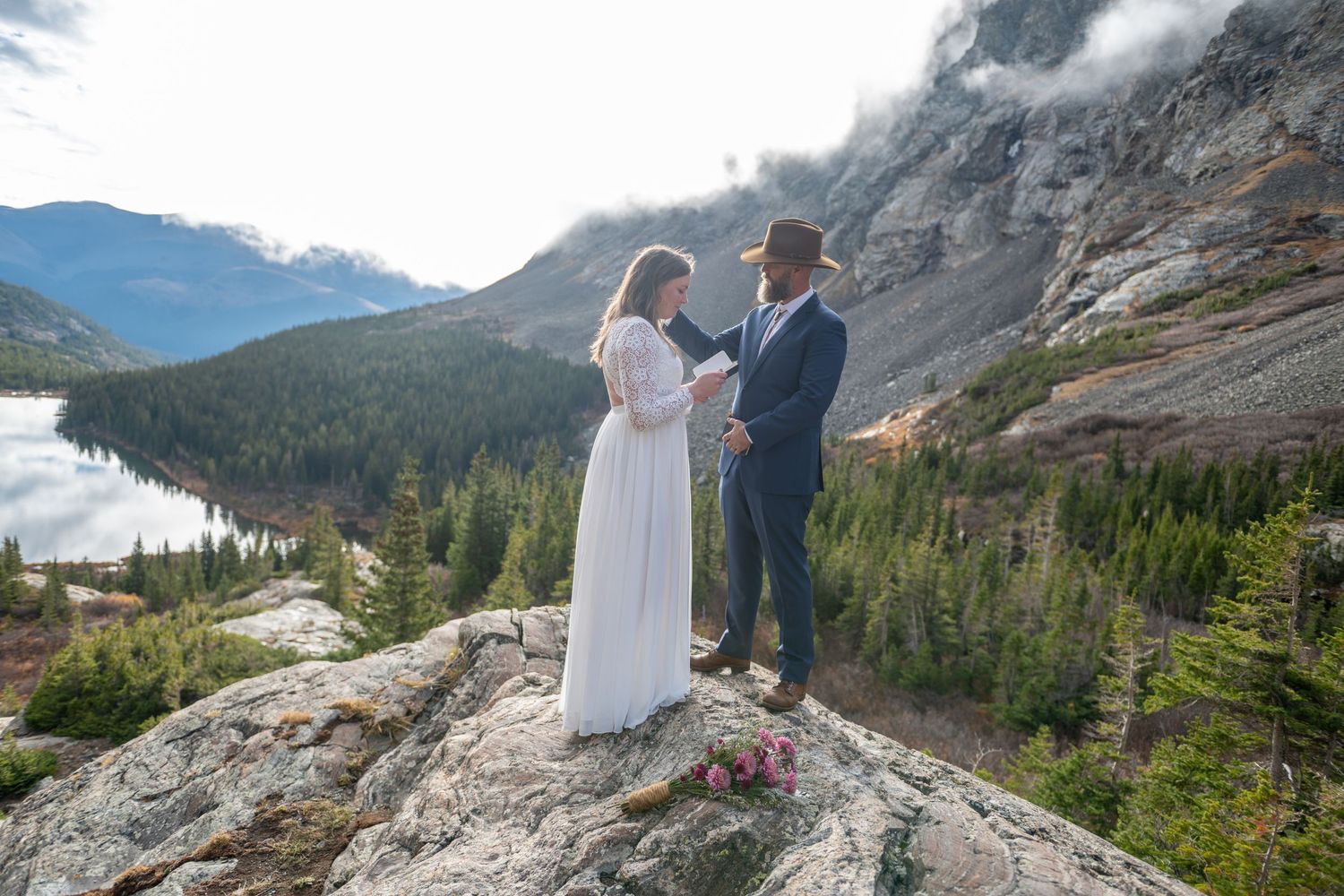 An eloping couple exchanges vows on a rocky mountain summit near Breckenridge with a stunning alpine lake and misty peaks as a  backdrop.