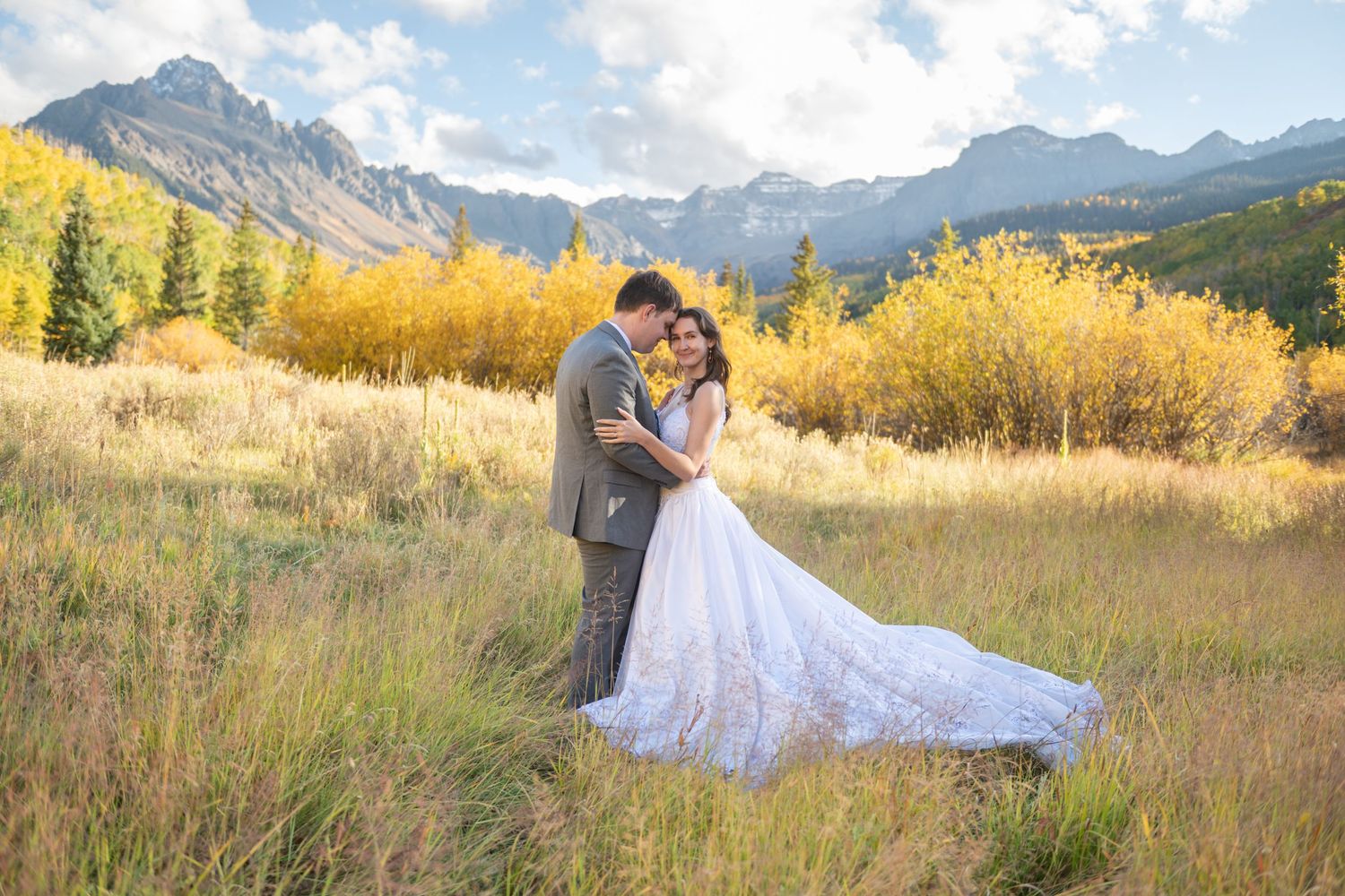 An eloping couple embracing in a mountain meadow with golden autumn foliage and rocky peaks near Ridgway for their wedding photo.