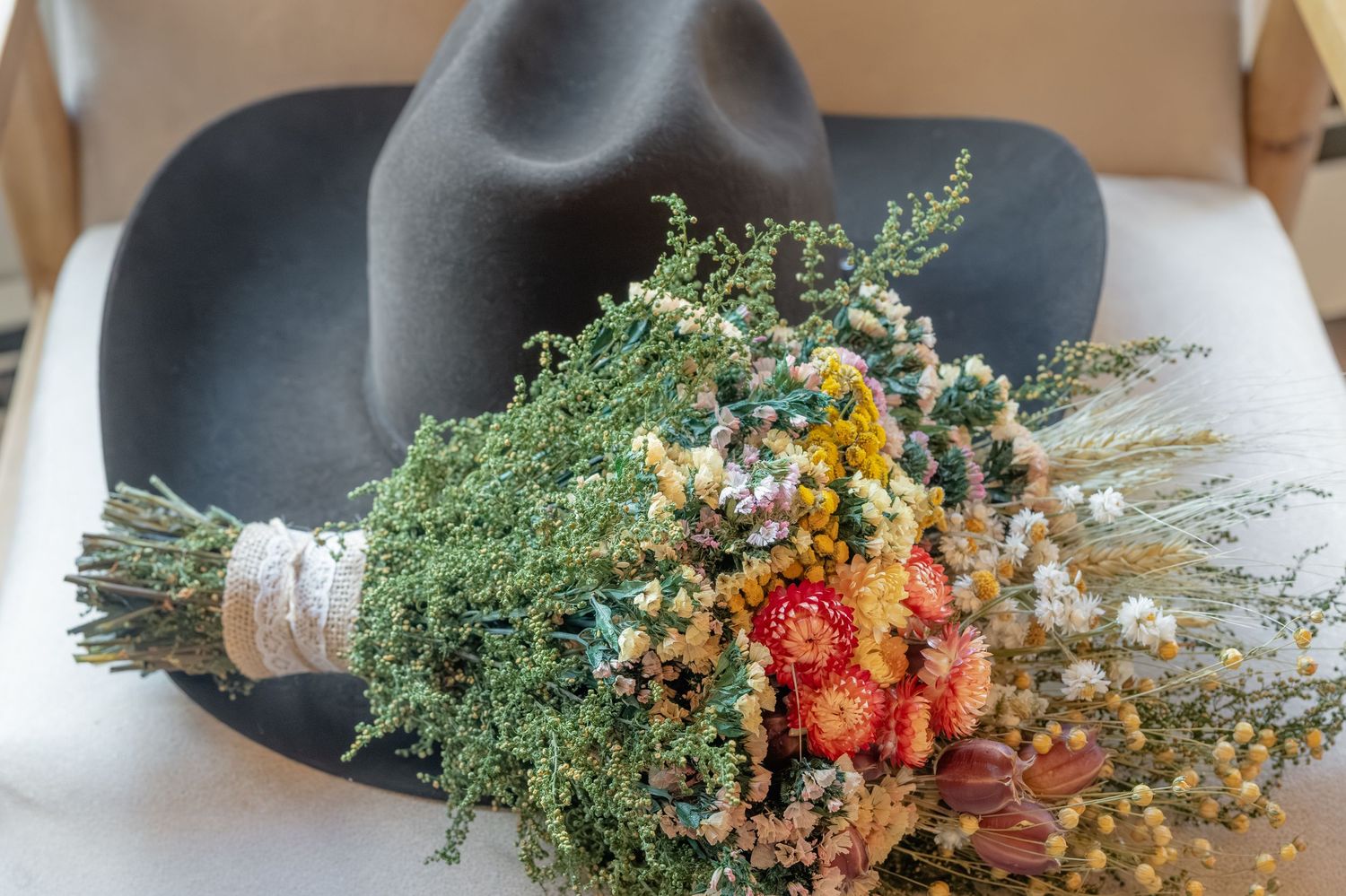 Rustic dried wildflower bouquet with red, yellow, and green blooms resting on a dark gray cowboy hat.