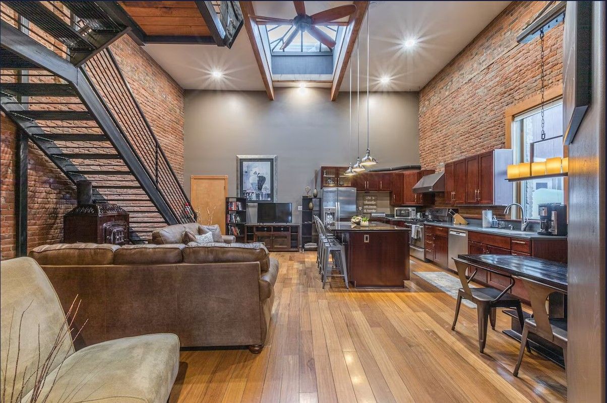 The inside of a modern loft Airbnb rental in Ouray showing the metal staircase, granite kitchen island, and leather couches.