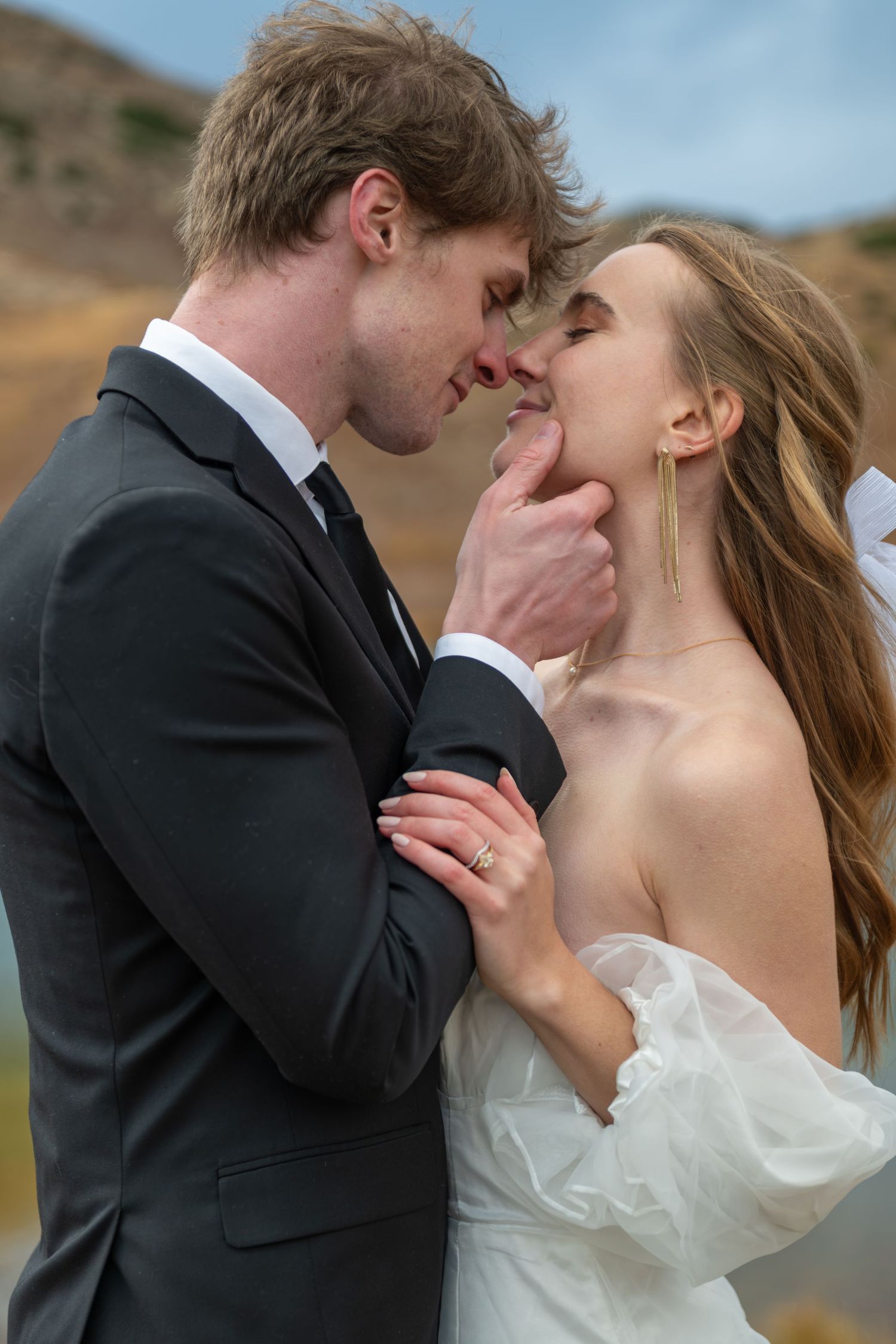 A bride and groom share an intimate moment outdoors after their elopement, with the groom gently holding the bride's chin.