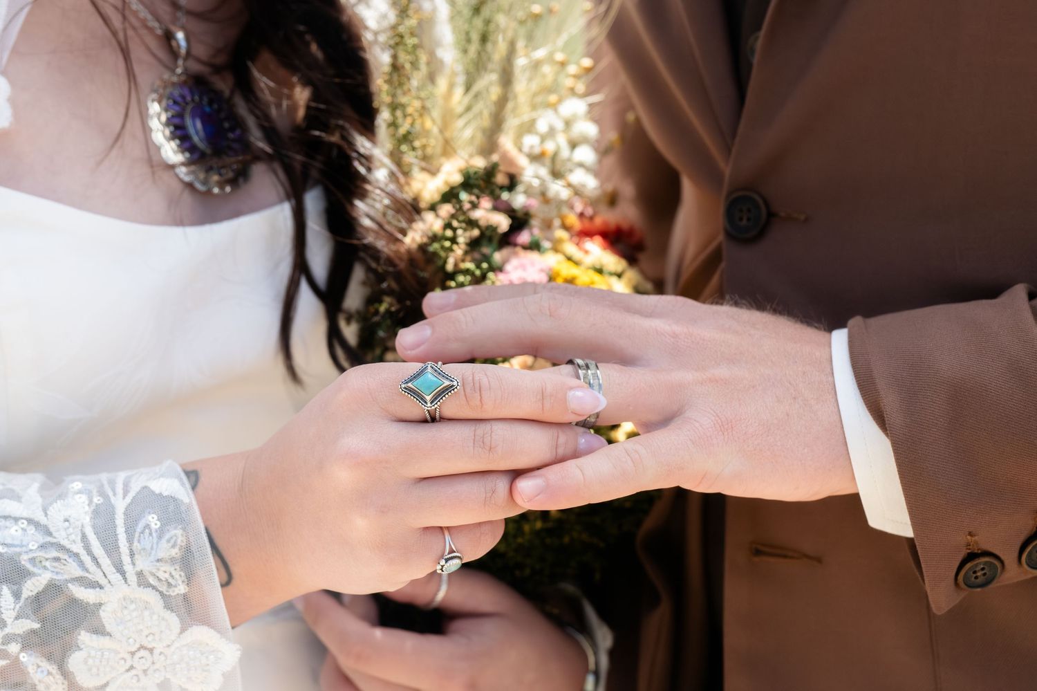 Close-up of bride and groom exchanging rings, featuring a turquoise gemstone ring and diamond bands at a wedding ceremony.