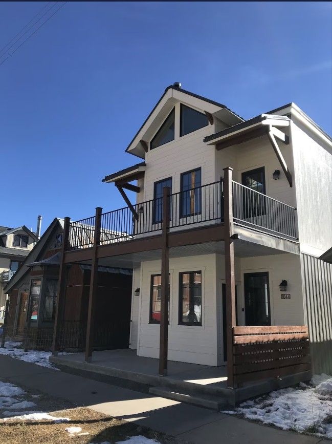 The outside of a two story white Airbnb rental property in Silverton  with a deck around the second story. Snow is on the ground.
