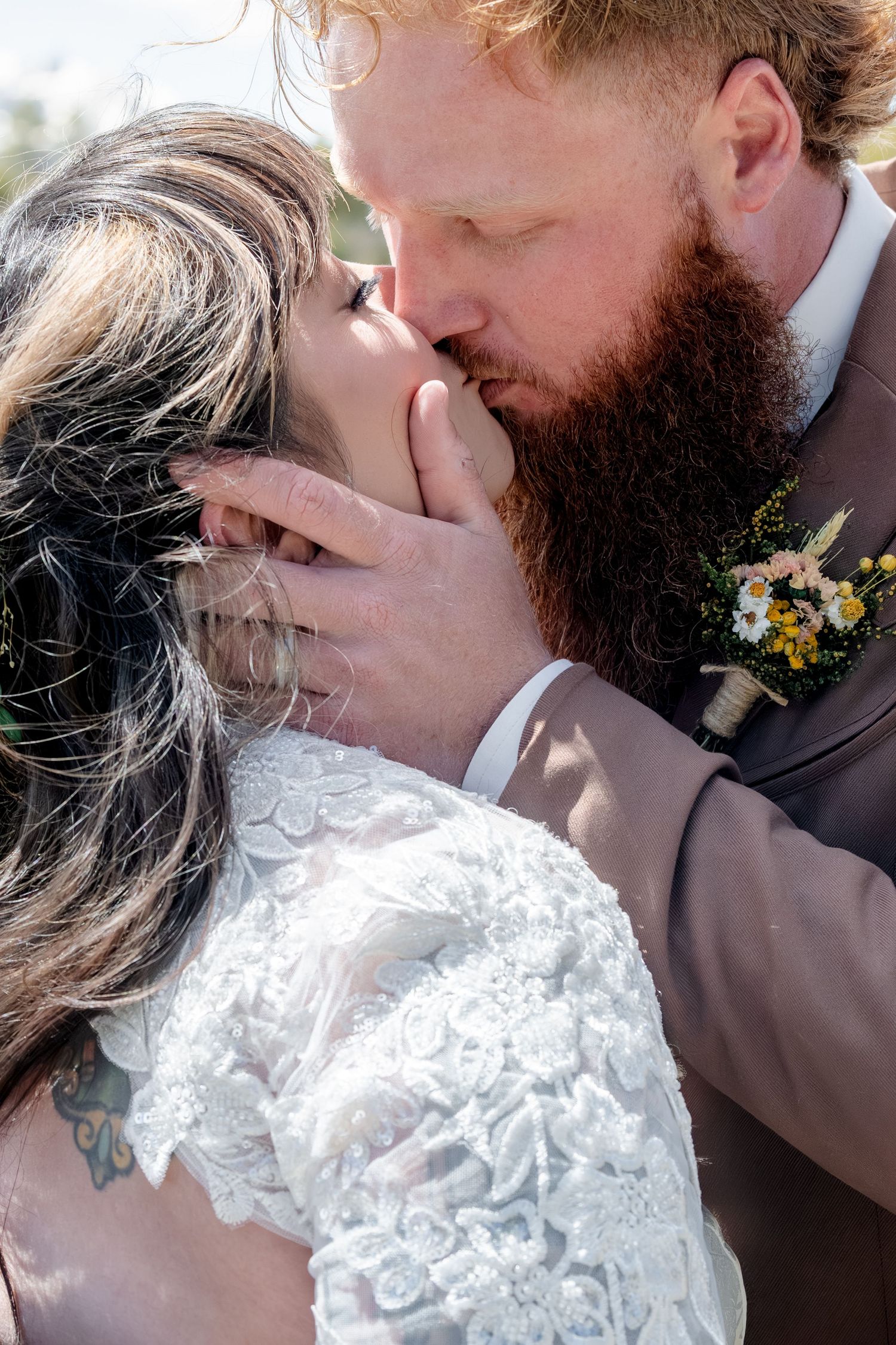 A bearded groom in a brown suit tenderly kisses his bride in a lace dress during their outdoor elopement wedding ceremony near Ridgway