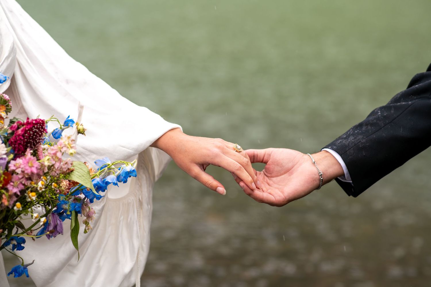 Bride and groom gently holding hands outdoors, bride wearing floral kimono sleeve holding colorful bouquet.