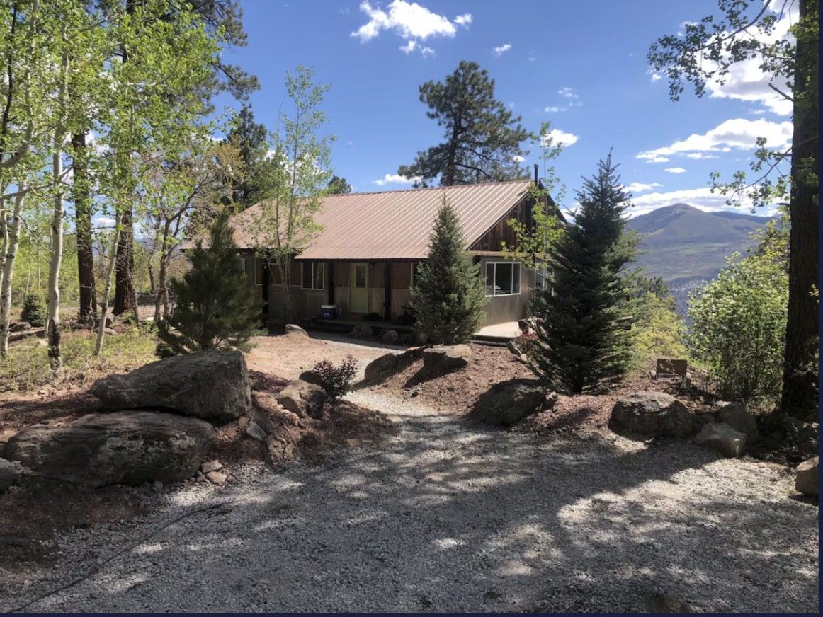 A photo of an Airbnb mountain property near Ouray with dirt paths, pine and aspen trees, and a rustic cabin in the distance.