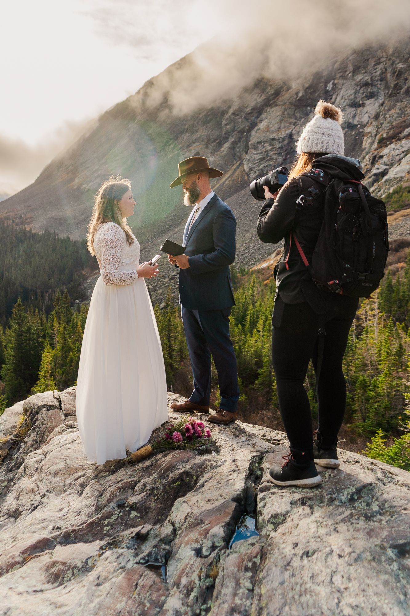 Couple exchanging vows at mountain elopement ceremony near Breckenridge on rocky summit with photographer capturing the moment.