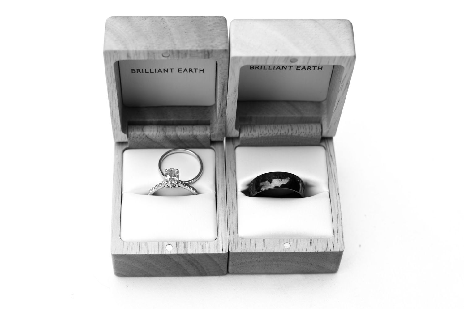 Two Brilliant Earth rings in wooden boxes, one diamond engagement ring and one dark gemstone ring, displayed side by side.
