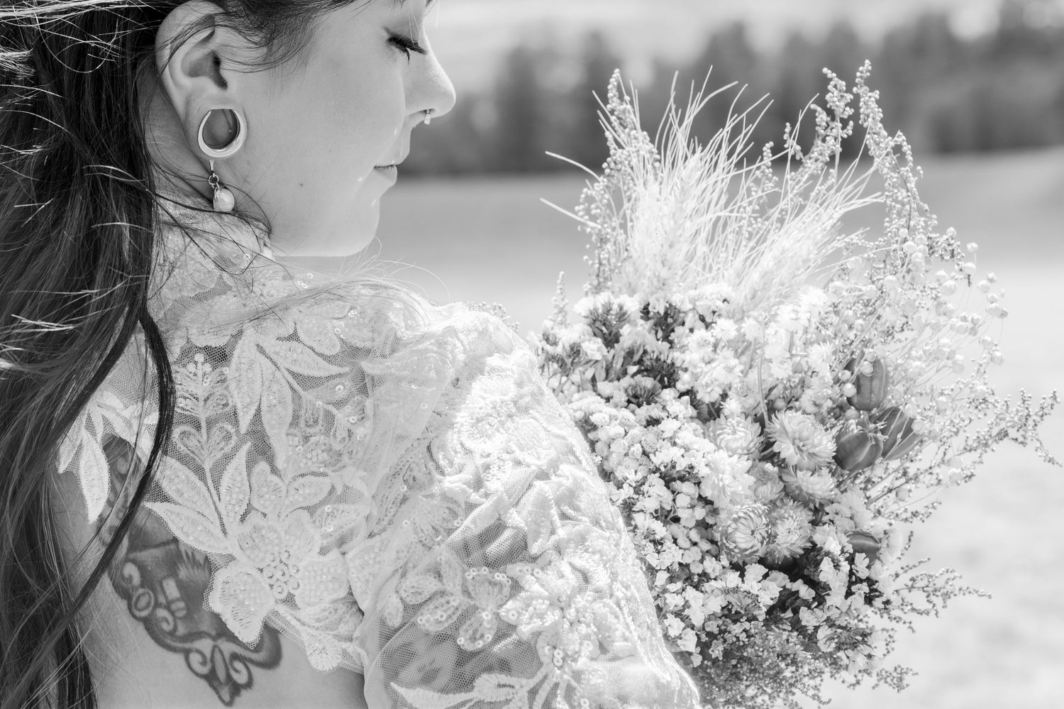Black and white photo of a tattooed bride in lace dress holding wildflower bouquet.
